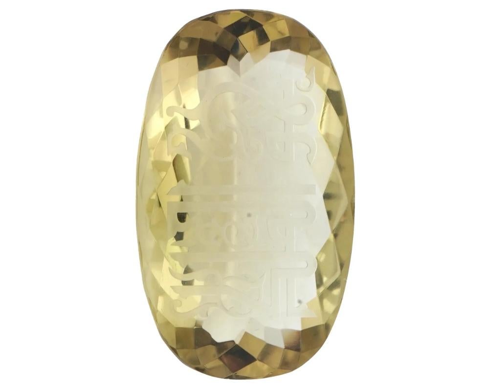 A large natural citrine gemstone with curved Arabic script on both sides. The gemstone features a faceted surface that enhances its brilliance, and it is elegantly displayed in a black velvet presentation box with a white satin interior. Antique and