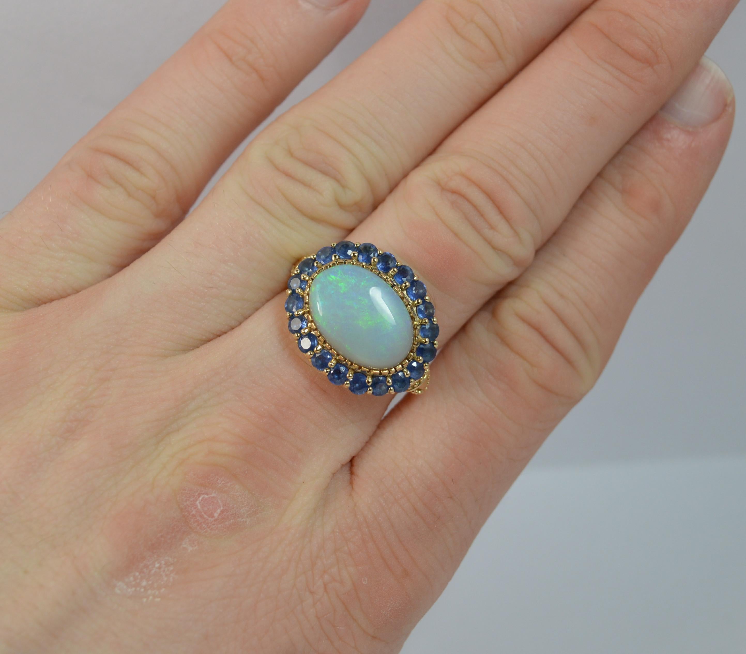 A stunning ladies cluster or cocktail ring.
SIZE ; N 1/2 UK, 7 US
A solid 9 carat yellow gold example.

Set with a single opal to the centre, 10mm x 14mm with blue and green undertone. 

Surrounding are beautifully blue round cut sapphires.

19mm x