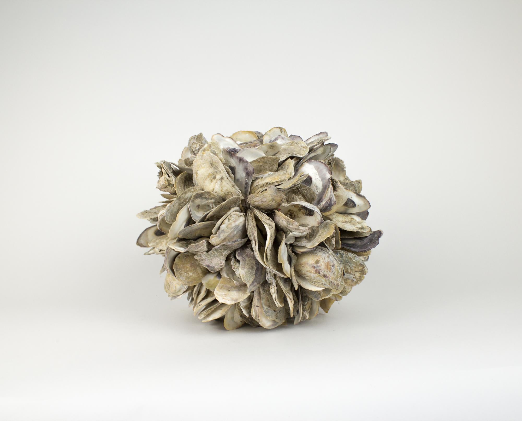 Large sphere sculpture made of natural oyster shells. Each shell is strung together with rope to creature a round shape. Natural texture and neutral colors will add texture to any sea or nautical themed room. Perfect size for large coffee table or