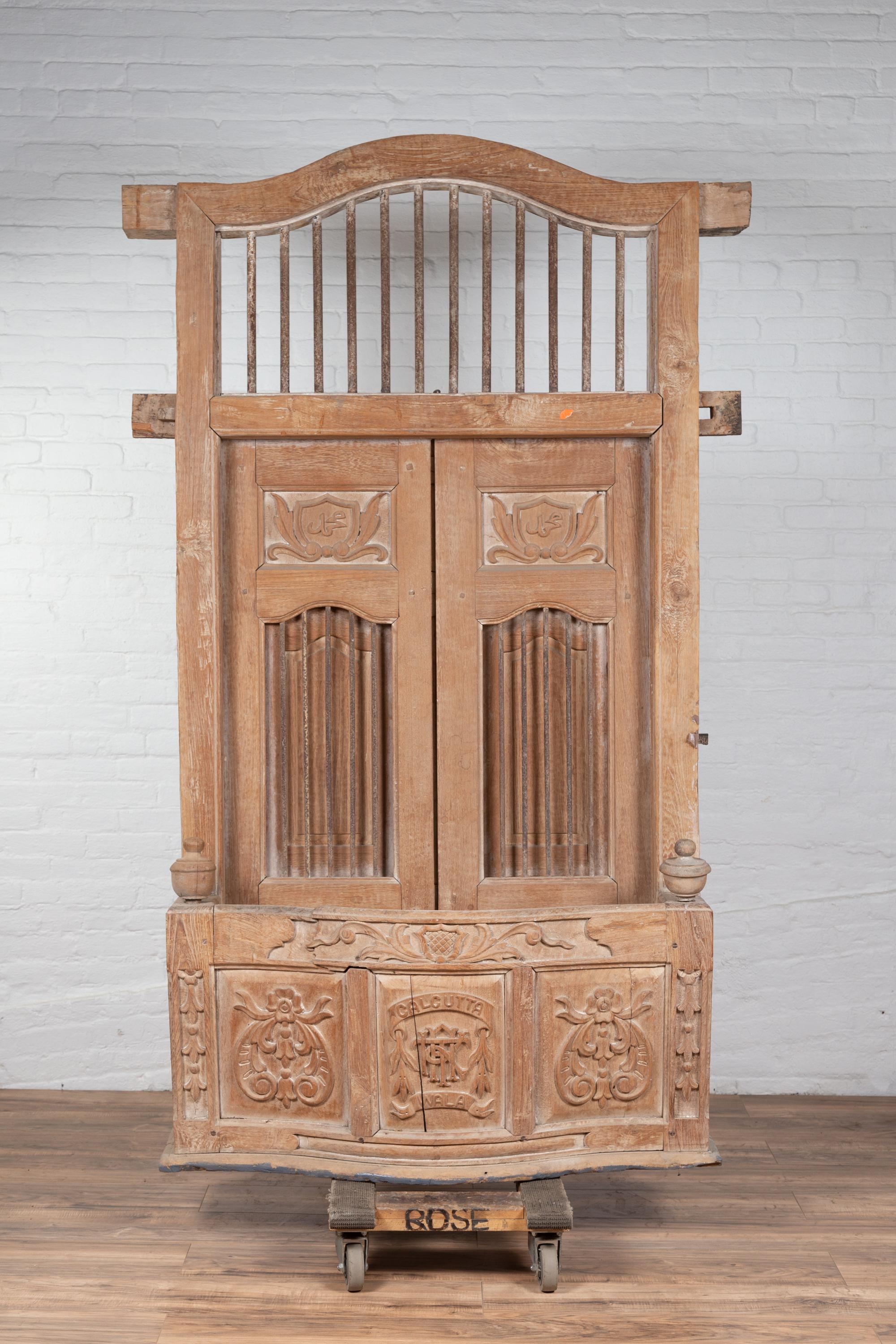 A large Indian hand carved wooden bonnet top window balcony from the early 20th century with rod motifs and foliage. Found in Indonesia, this window balcony captivates our attention with its large proportions and natural finish. Adorned with a