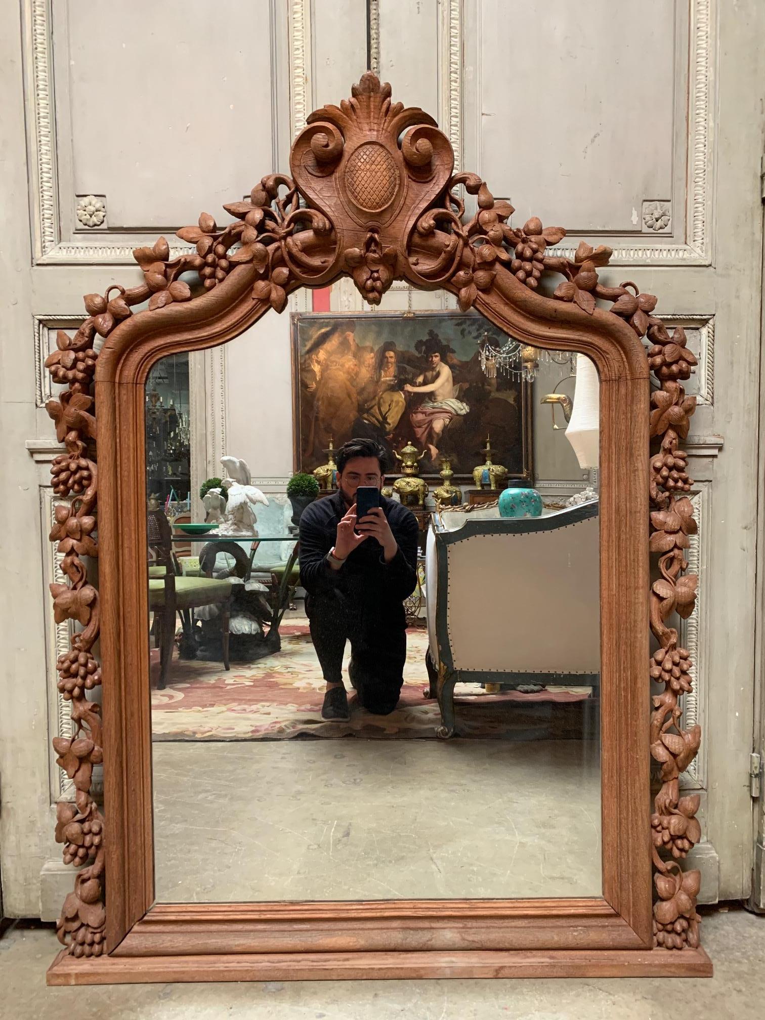 This large intricately carved trumeau mirror is bordered by rich voluble decor of leaves and bunches of grape clusters on twig, vine and foliage. At the top center it features a beautifully carved and detailed cartouche.