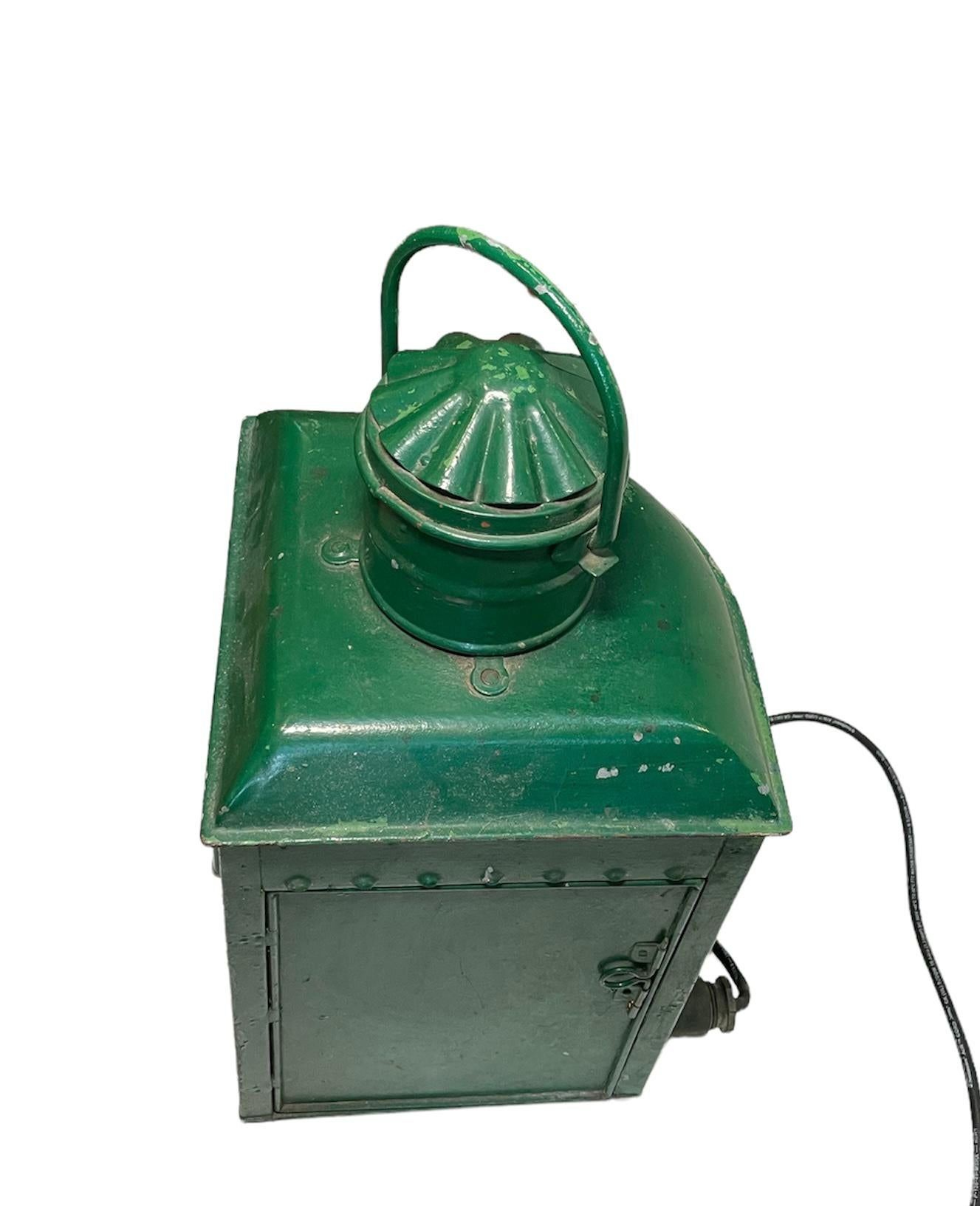 This is a former large oil nautical lantern. It depicts a metal port ship’s lantern painted green with a blue glass shade. It is electrified.