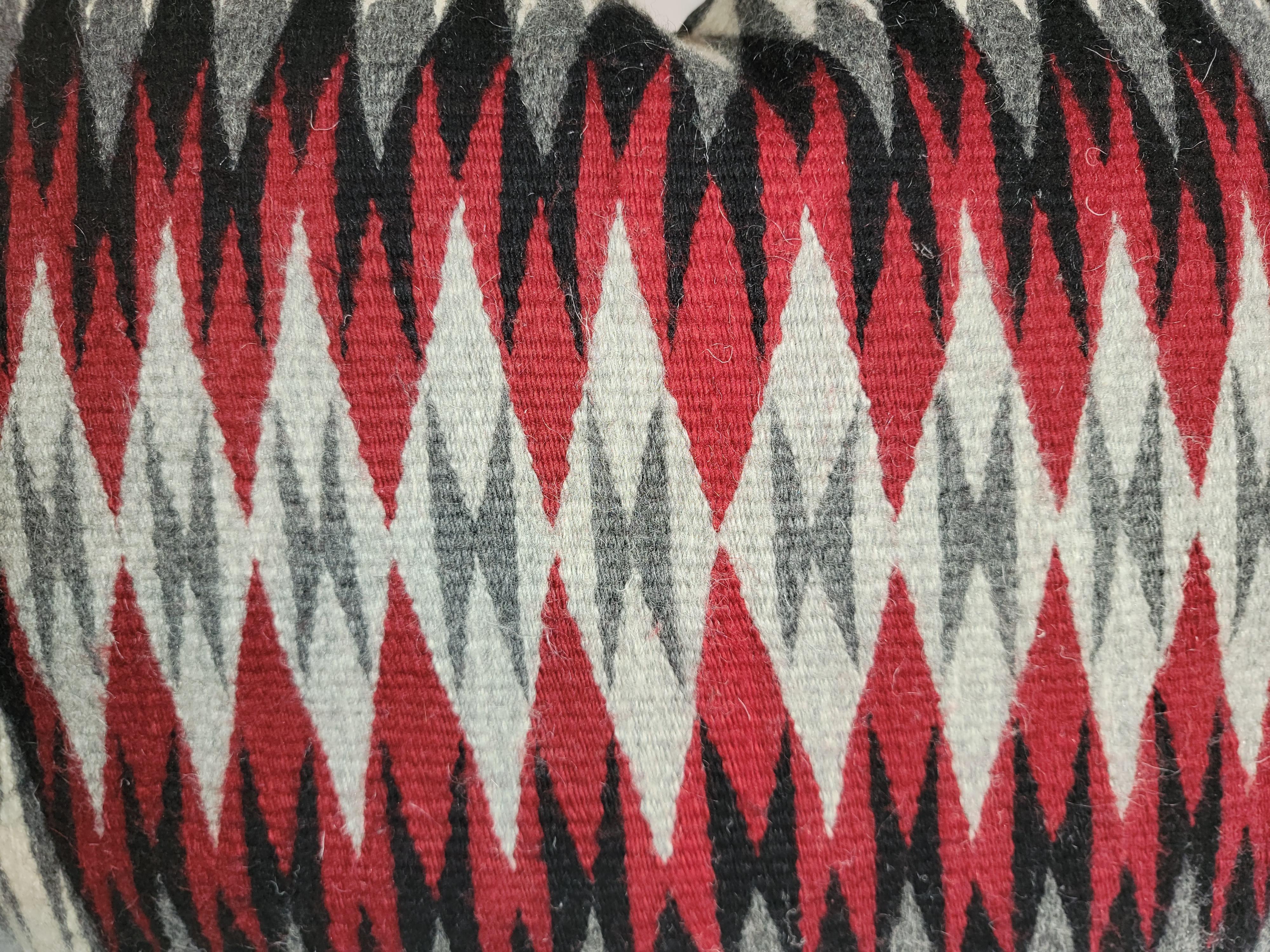Grand oreiller en laine Navajo tissée à motif d'œil en puzzle éblouissant avec des noirs et des rouges profonds qui fournissent une palette de couleurs forte. Ces couleurs représentent généralement la nature bonne et mauvaise du monde, toujours en