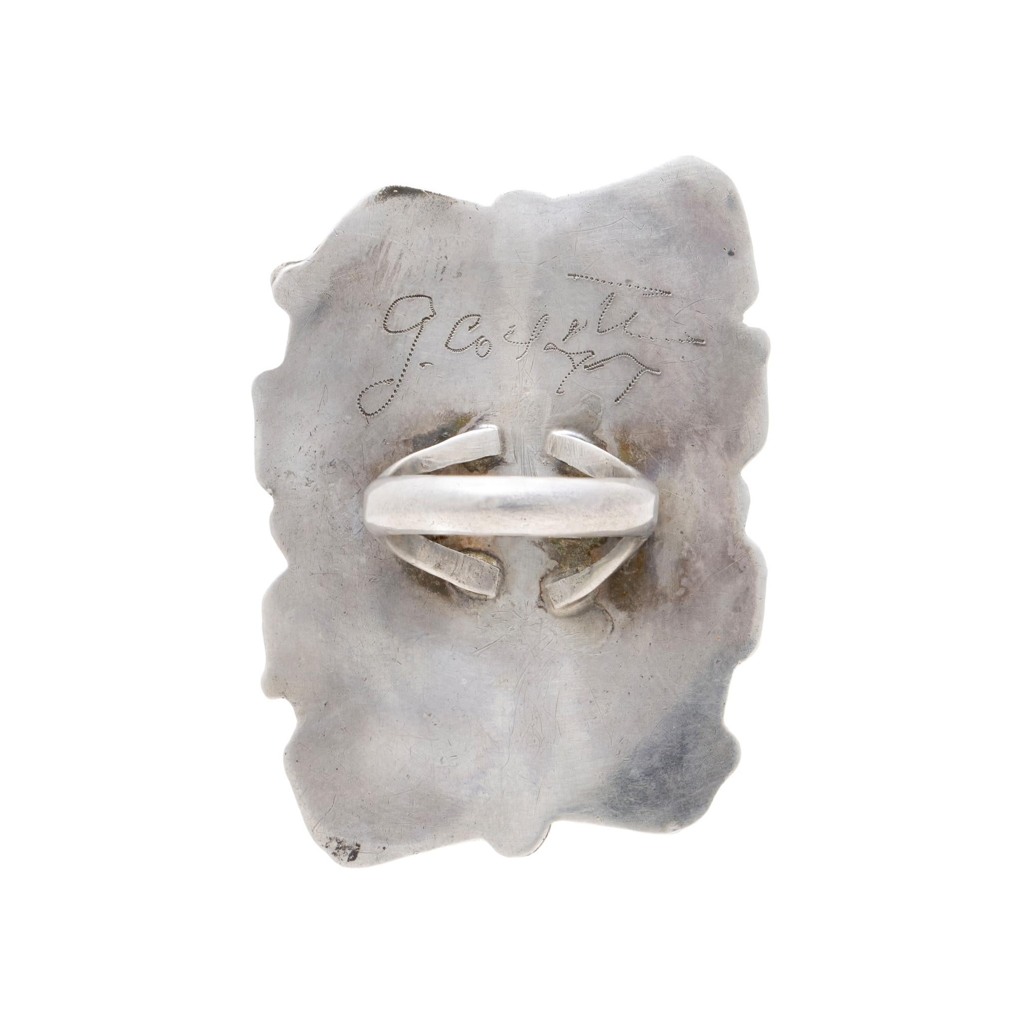 Large single stone Navajo King's Manassa turquoise ring. With twisted rope, feather, and scroll border over shadowbox backdrop. Scrollwork frames the oval stone into a square shape. Stone features a deep blue color with marbled matrix of deep blue,