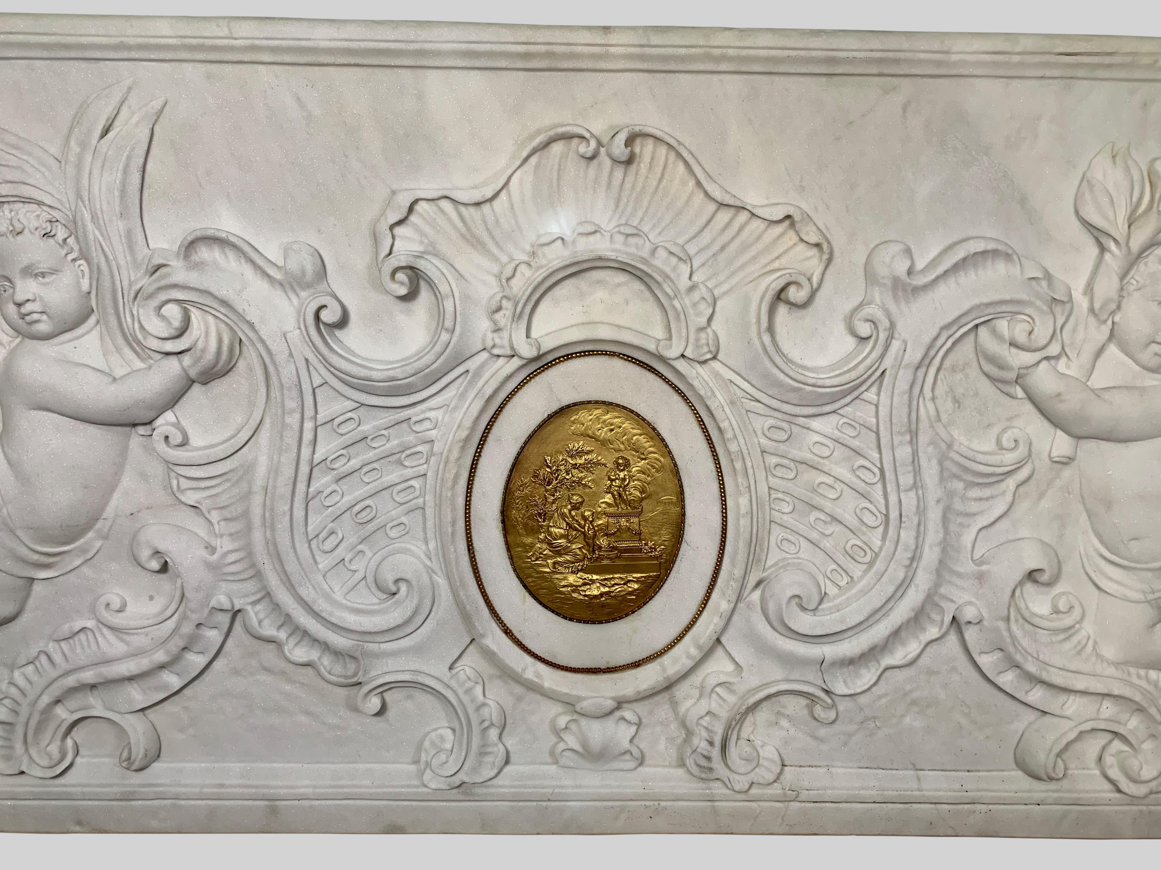 A monumental 19th century French hand carved white marble architectural bas-relief depicting two floating cherubs / cupids supporting a cartouche. The cartouche centered by a detailed oval gilt bronze plaque depicting figures in classical