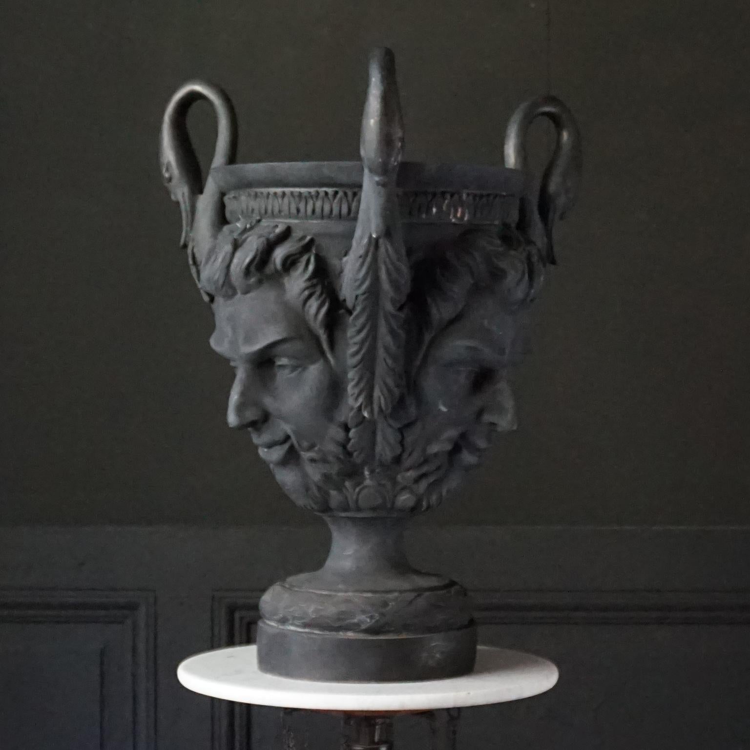 This heavy blackened brass jardiniere vase or planter is very impressive in size and in depiction.
Look at these three handles in the shape of swan neck and the detailed ornamental mascaron sater or faun faces. This will be an eye catcher for sure
