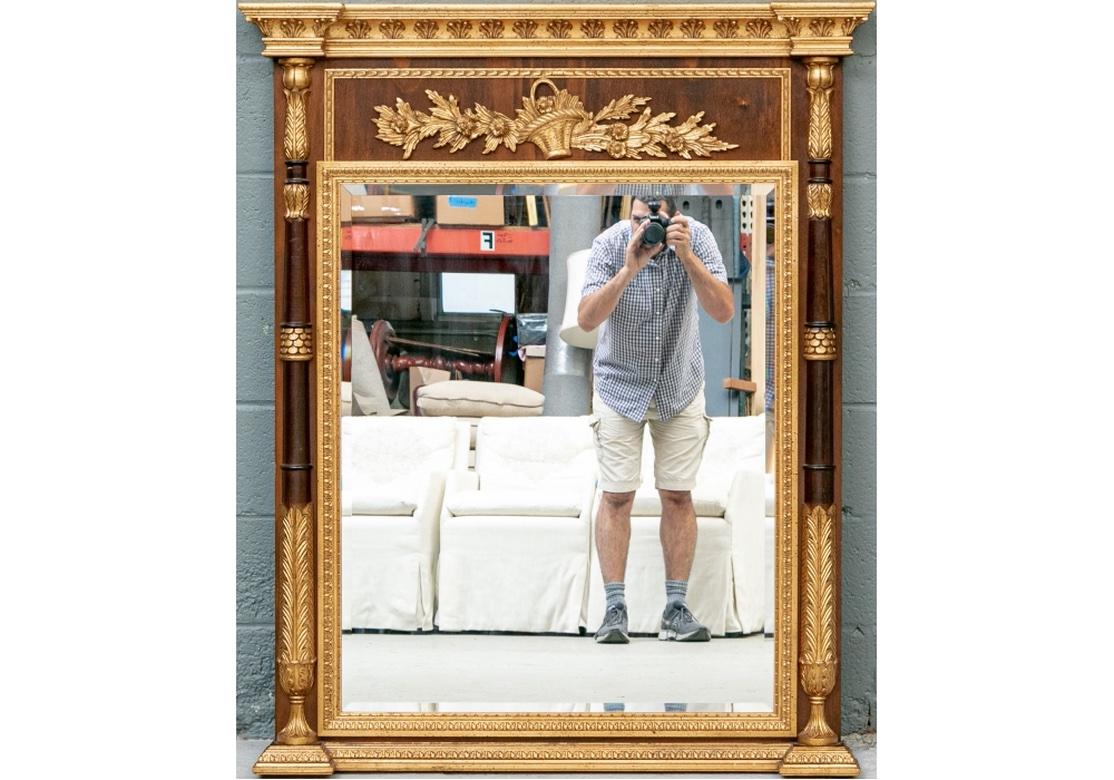 A large and striking Neoclassical style mirror crafted with gilt palmettes on the cornice and frieze with basket of flowers and leaves. The segmented half column supports turned with lovely gilt leafy details top and bottom. The inner surround and