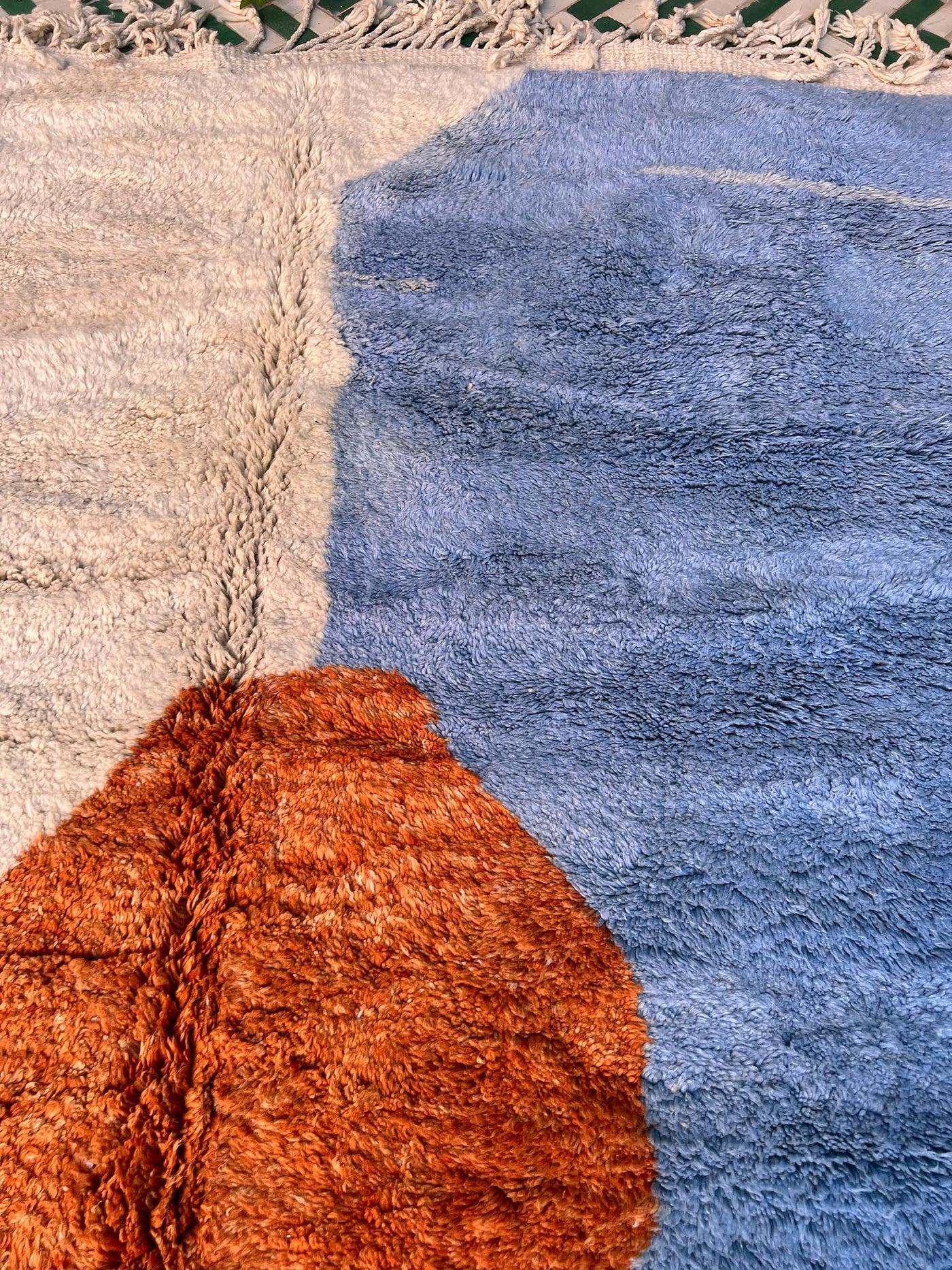 This large, modern handwoven Moroccan rug was made by hand by skilled artisans in the Atlas Mountains. It features a high quality, neutral cream wool base with a subtle, multi-colored abstract design reminiscent of a sun setting over water. Handmade