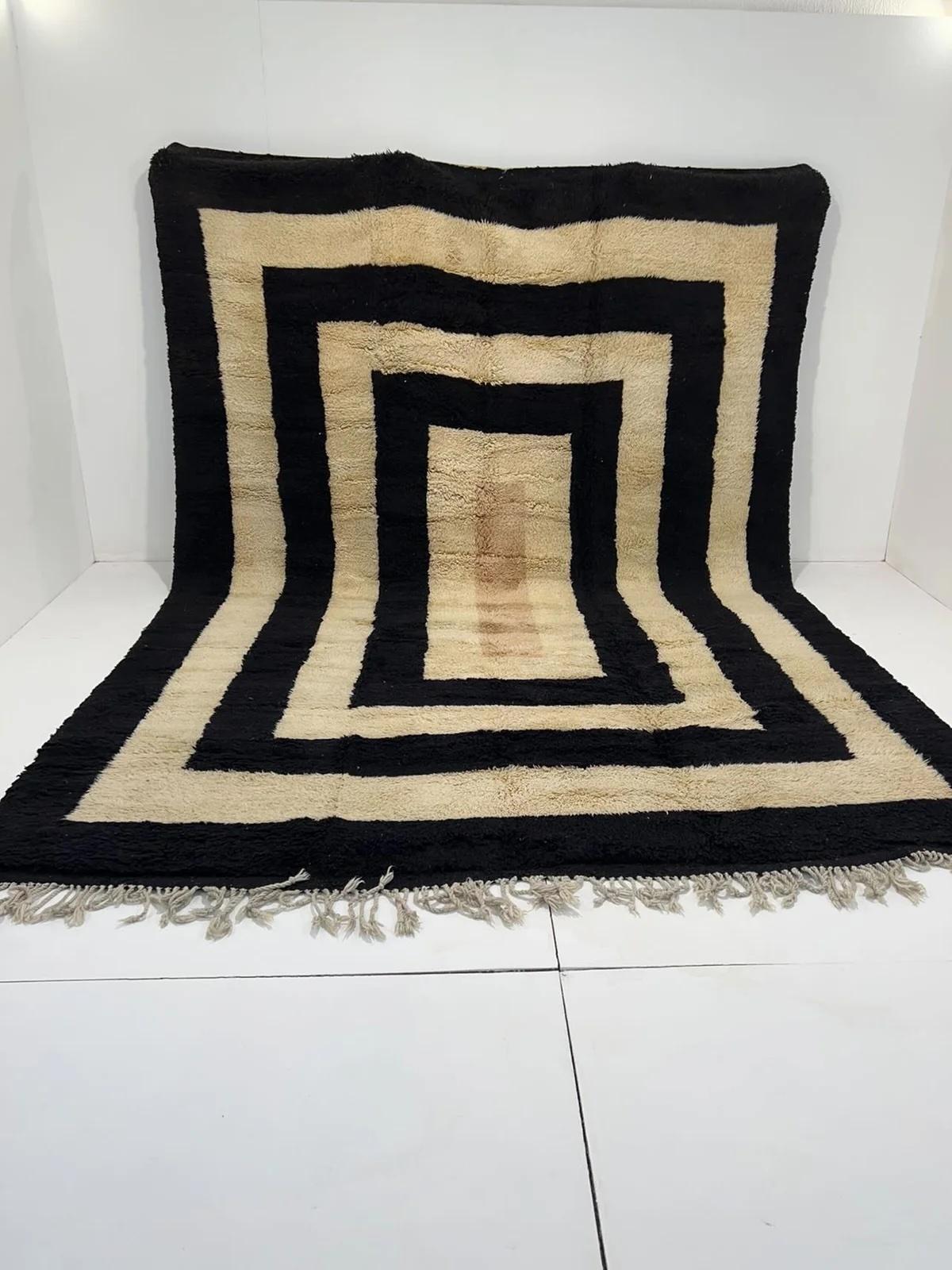 Questo grande tappeto marocchino neutro tessuto a mano è stato realizzato da abili artigiani nelle montagne dell'Atlante. È caratterizzato da una calda lana M'Rirt di alta qualità, con un bordo in lana nera che si ripete in modo audace. Il design è