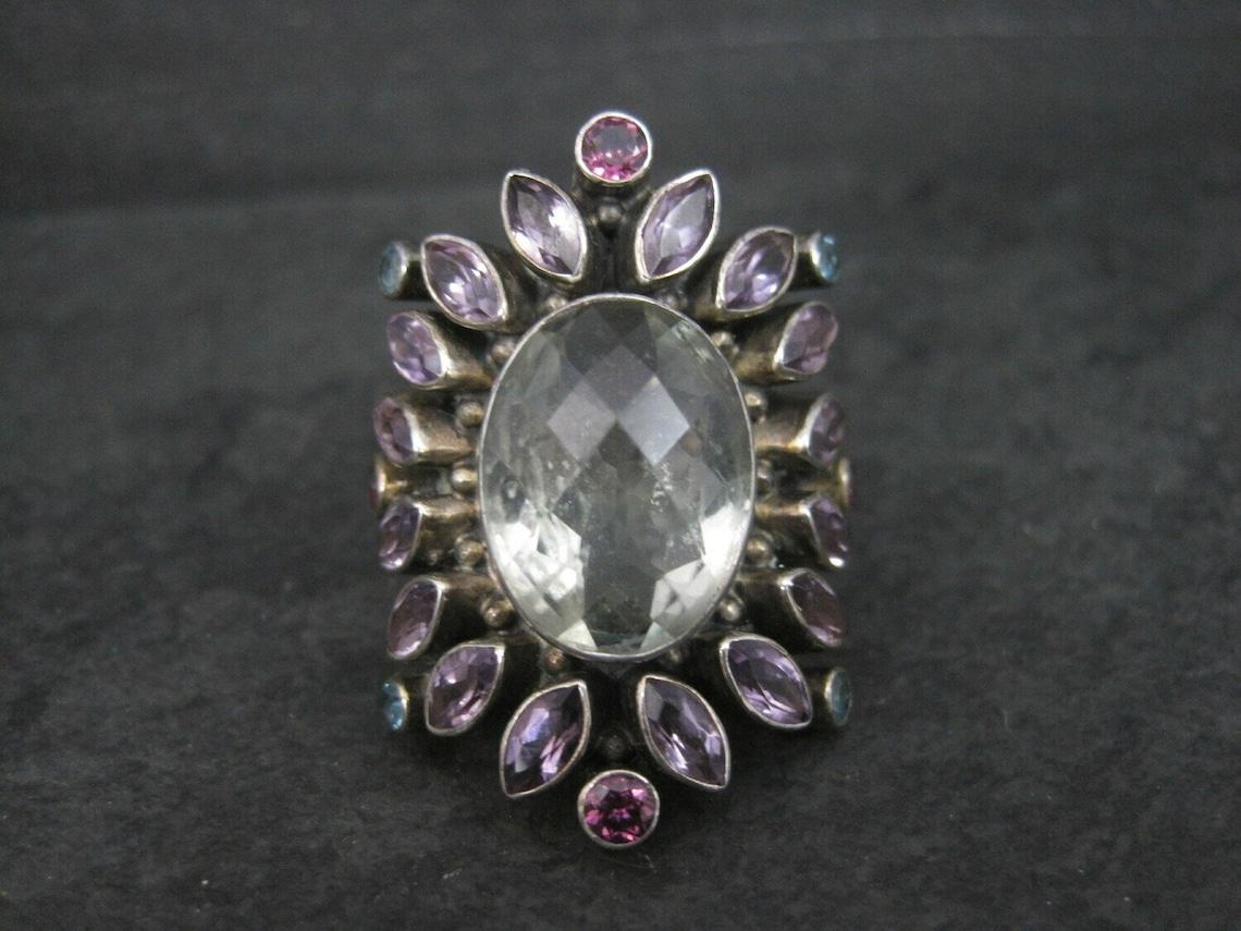 This gorgeous Nicky Butler ring is limited edition - #475 of 600.

It is sterling silver and features a 12x16 oval prasiolite accented by a halo of amethysts, blue topaz and rhodolite garnets.

The face of this ring measures 1 3/8 inches north to