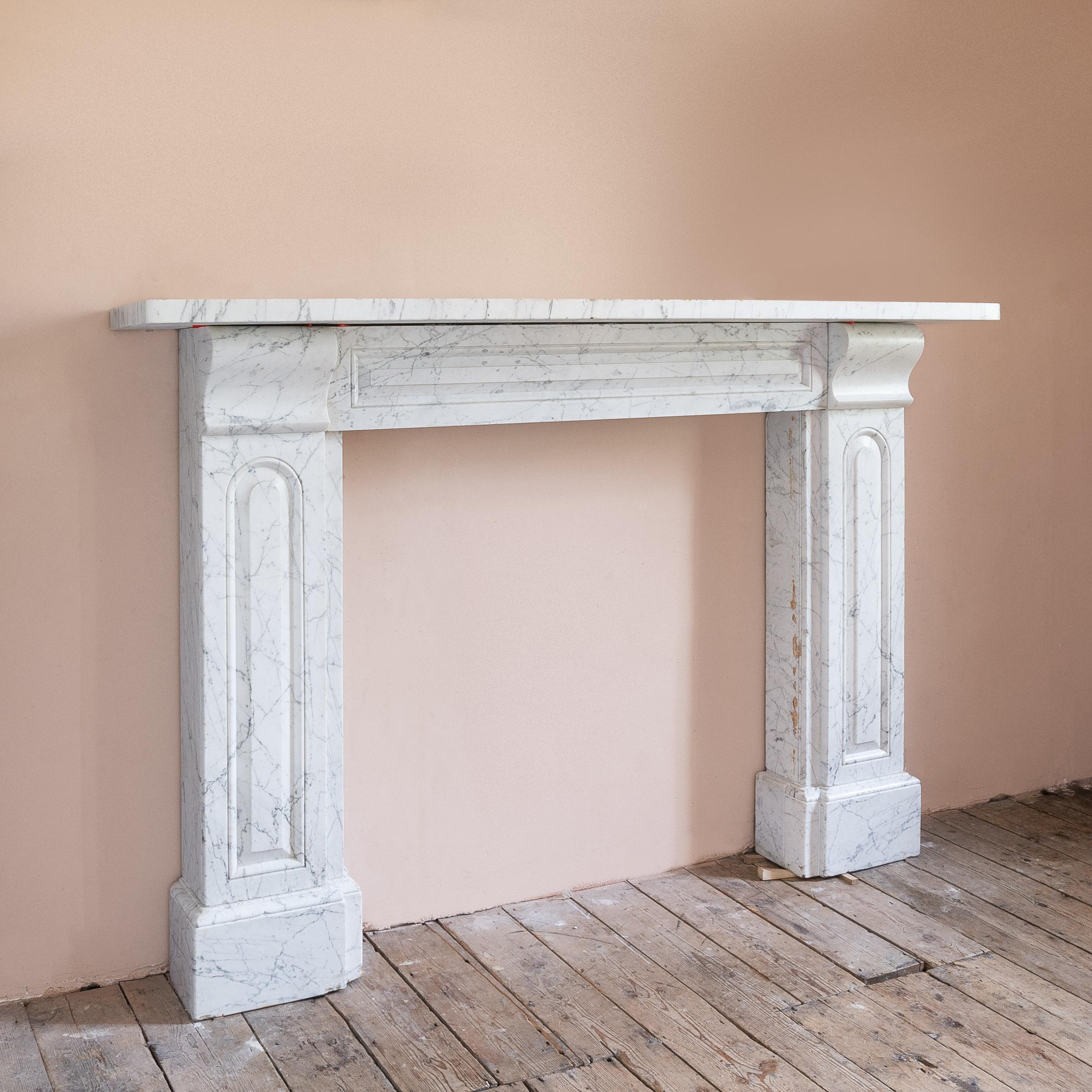 Grande camino in marmo di Carrara del XIX secolo, 1825-1840 circa, con mensole semplici che fiancheggiano il fregio a pannelli, gli stipiti con ulteriori pannelli ad arco, su piedi a blocco.

Dimensioni:	118 cm (46½