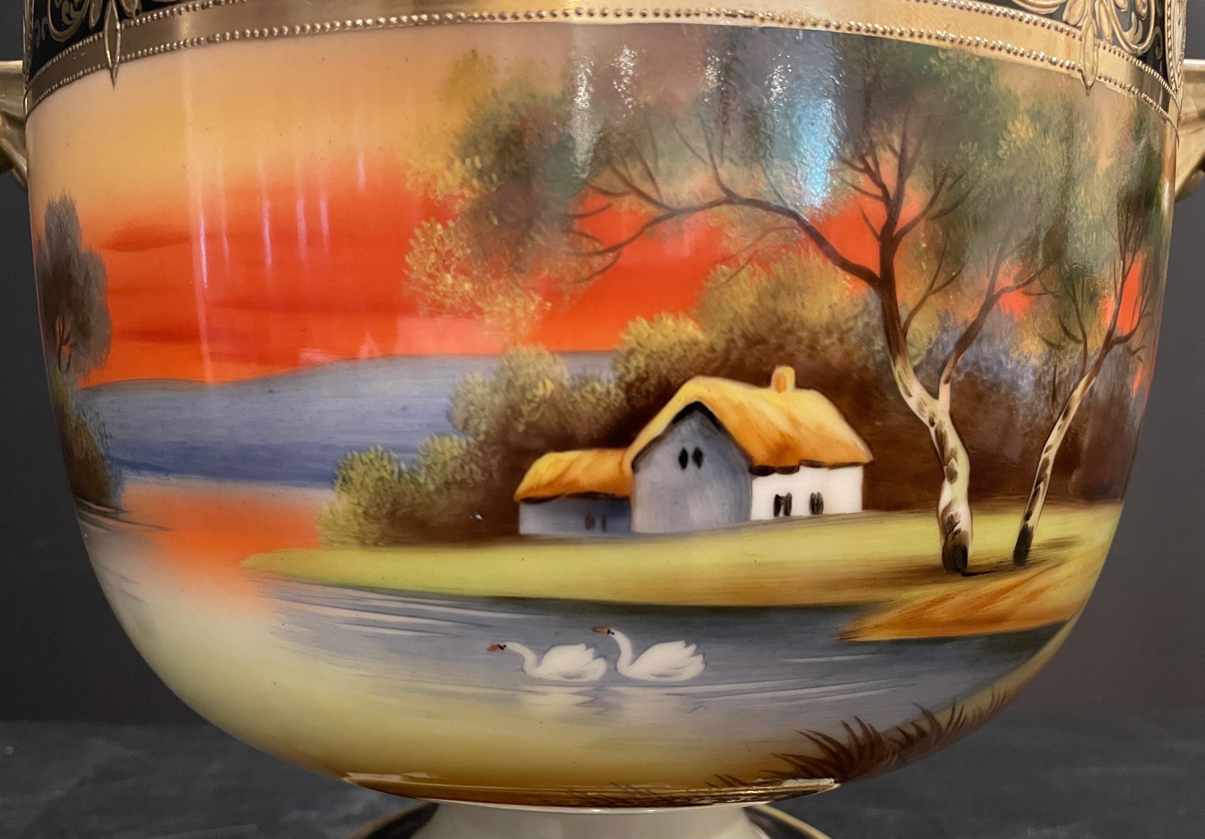 Colorful and large two piece footed pedestal centerpiece bowl from Noritake. Fiery oranges of sunset on a lakeside cottage scene with swans and trees. Luster gold interior. Cobalt blue and gilt accents.
Interior diameter. 10