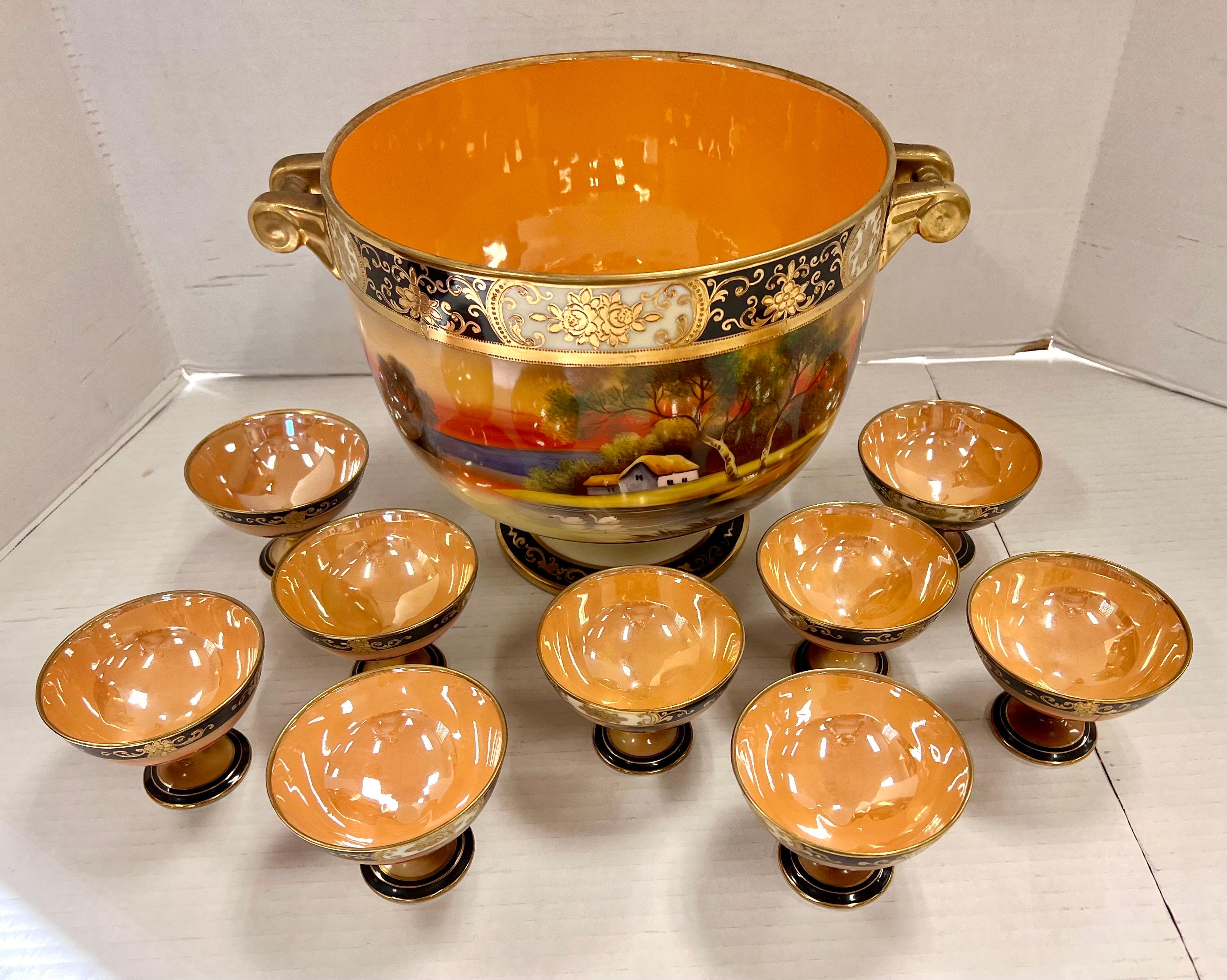 Colorful and large footed pedestal centerpiece punch bowl with 9 matching cups.  Stunning hand painted scenery of sunset on a lake cottage scene complete with swans and trees. Features luster gold interior with cobalt blue and gilt accents.  All