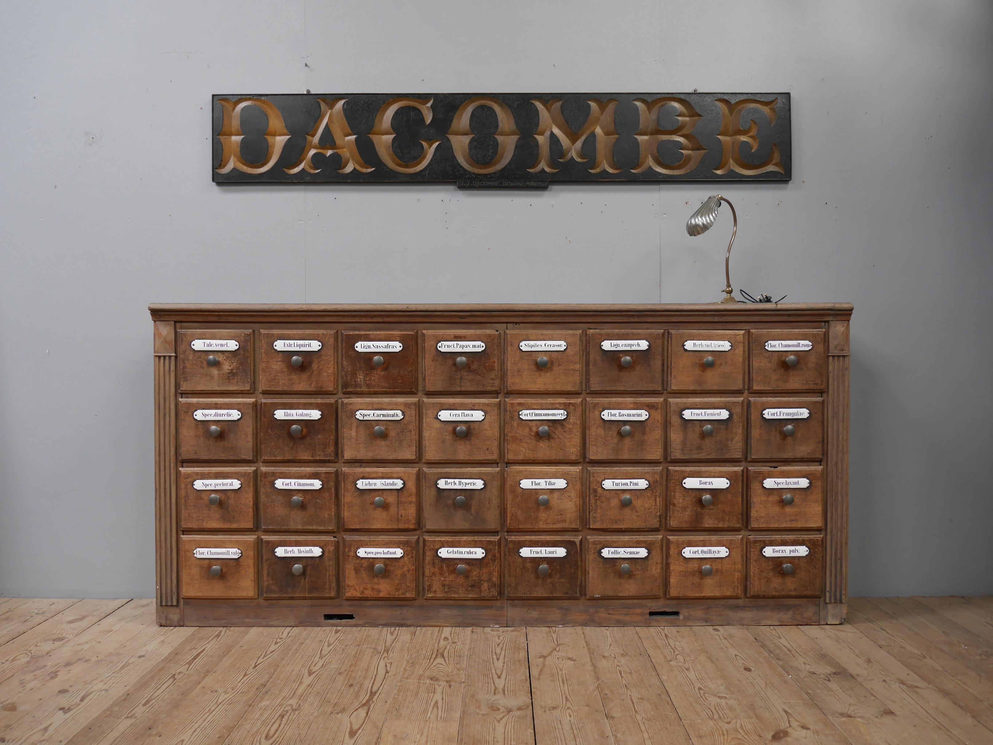 A large bank of thirty two antique oak pharmacy drawers.
In solid oak throughout with the most wonderfully detailed original vitreous enamel plaques to the drawer fronts, cast iron handles & a delightfully untouched patina. Of good scale, with the