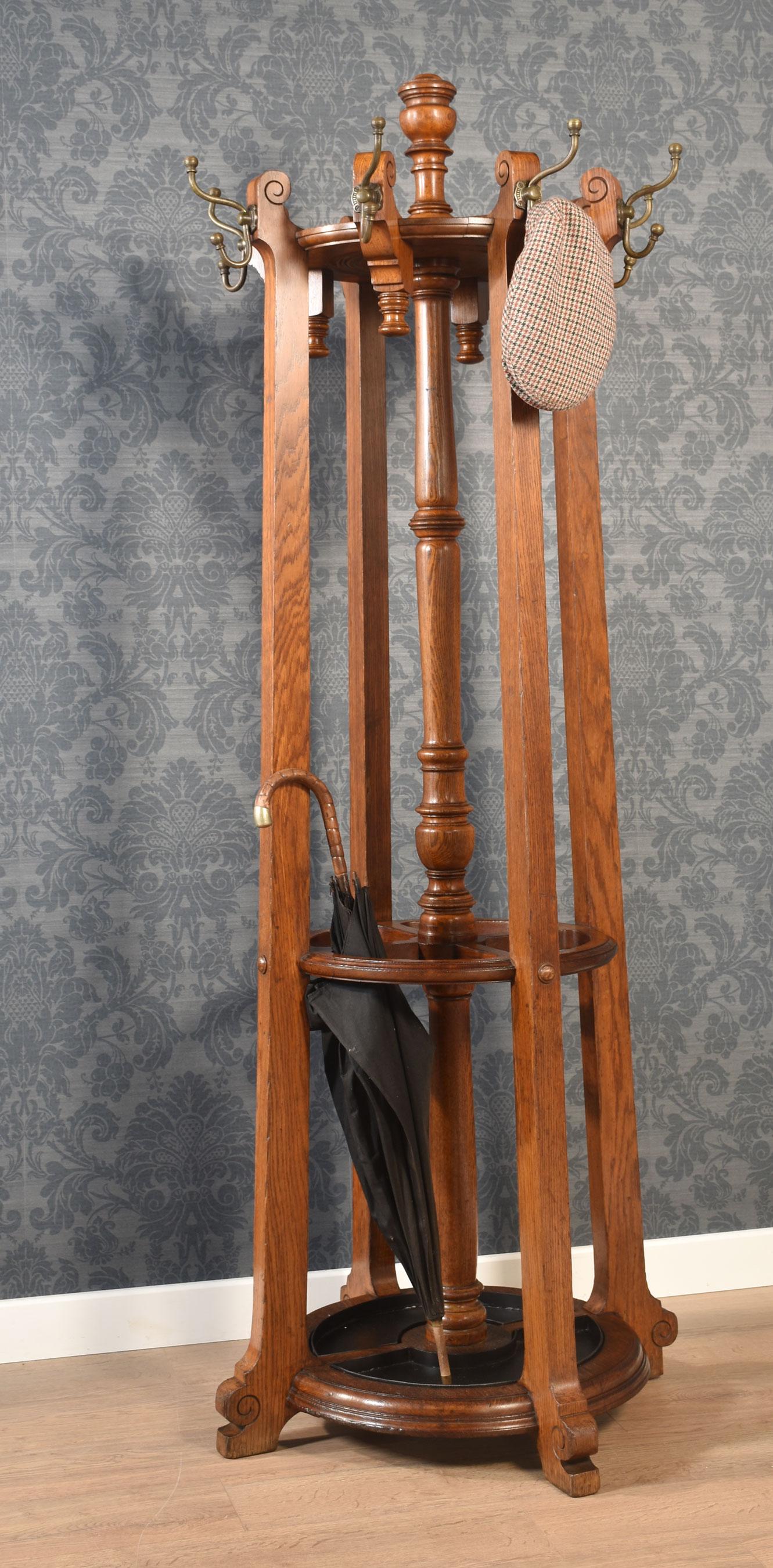 Porte-chapeaux et porte-parapluies en chêne, de forme circulaire avec un fleuron sculpté au-dessus de huit patères réglables en laiton bien coulé reposant sur des montants en chêne massif. Le porte-parapluie, divisé en quatre, est doté de plateaux