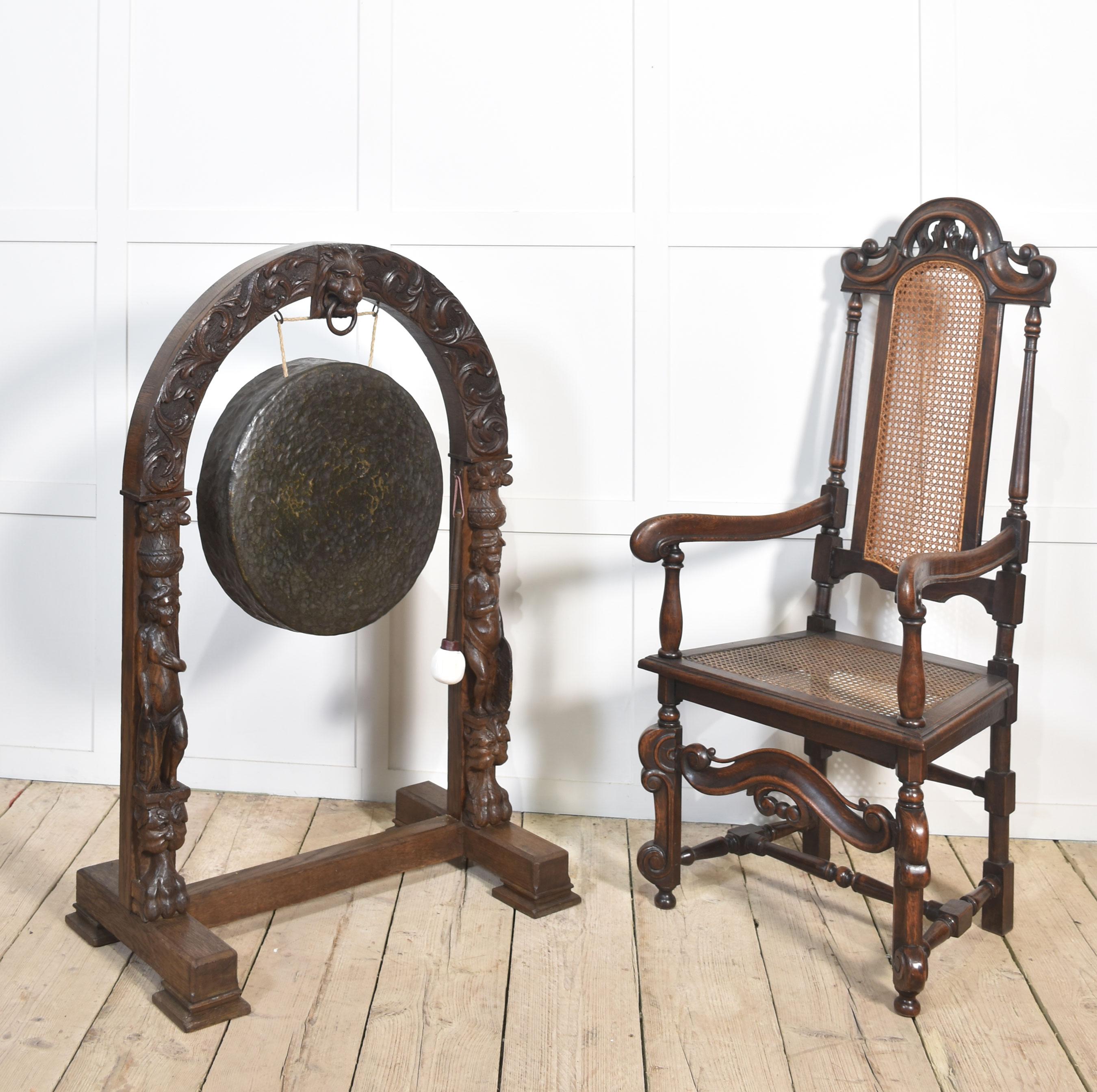 Grand gong de table en chêne, le sommet en arc avec une tête de masque de lion et un anneau suspendu, entouré de rinceaux et de feuillages sculptés, au-dessus de deux personnages soutenant le gong en laiton d'origine. Le tout surélevé sur un