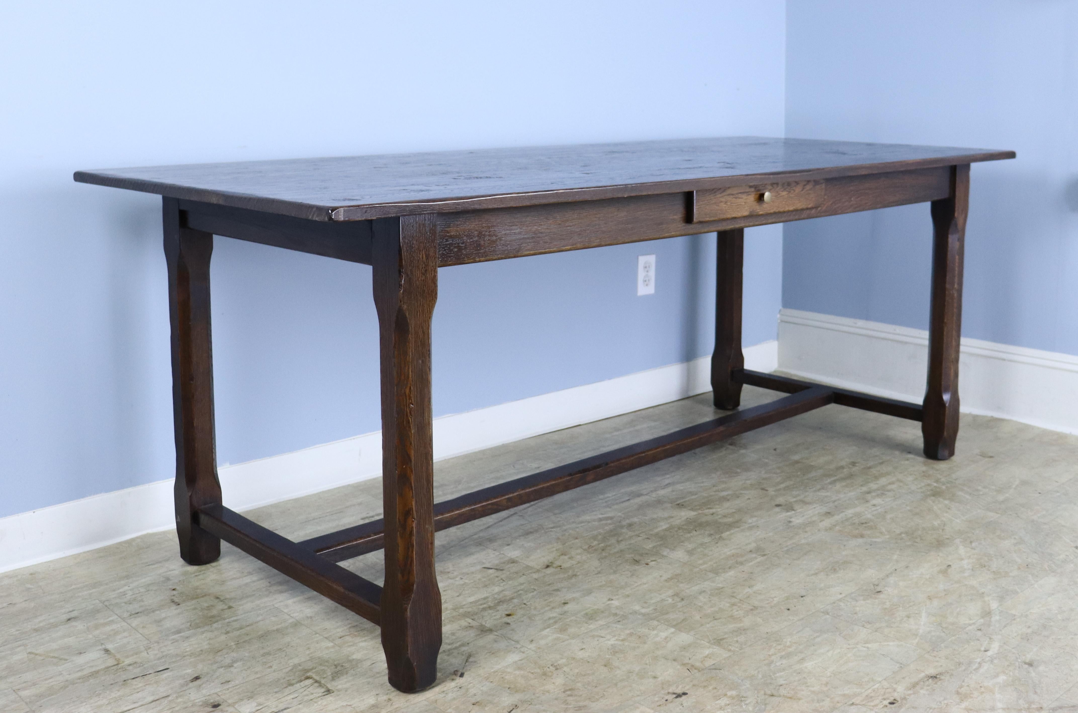 A large oak trestle based vintage farm table with the look of an antique. Good dark oak color and vivid grain. Immaculate and clean with a single drawer for interest.   Apron height of 25.75″ is quite generous, and there are 61″ between the legs on