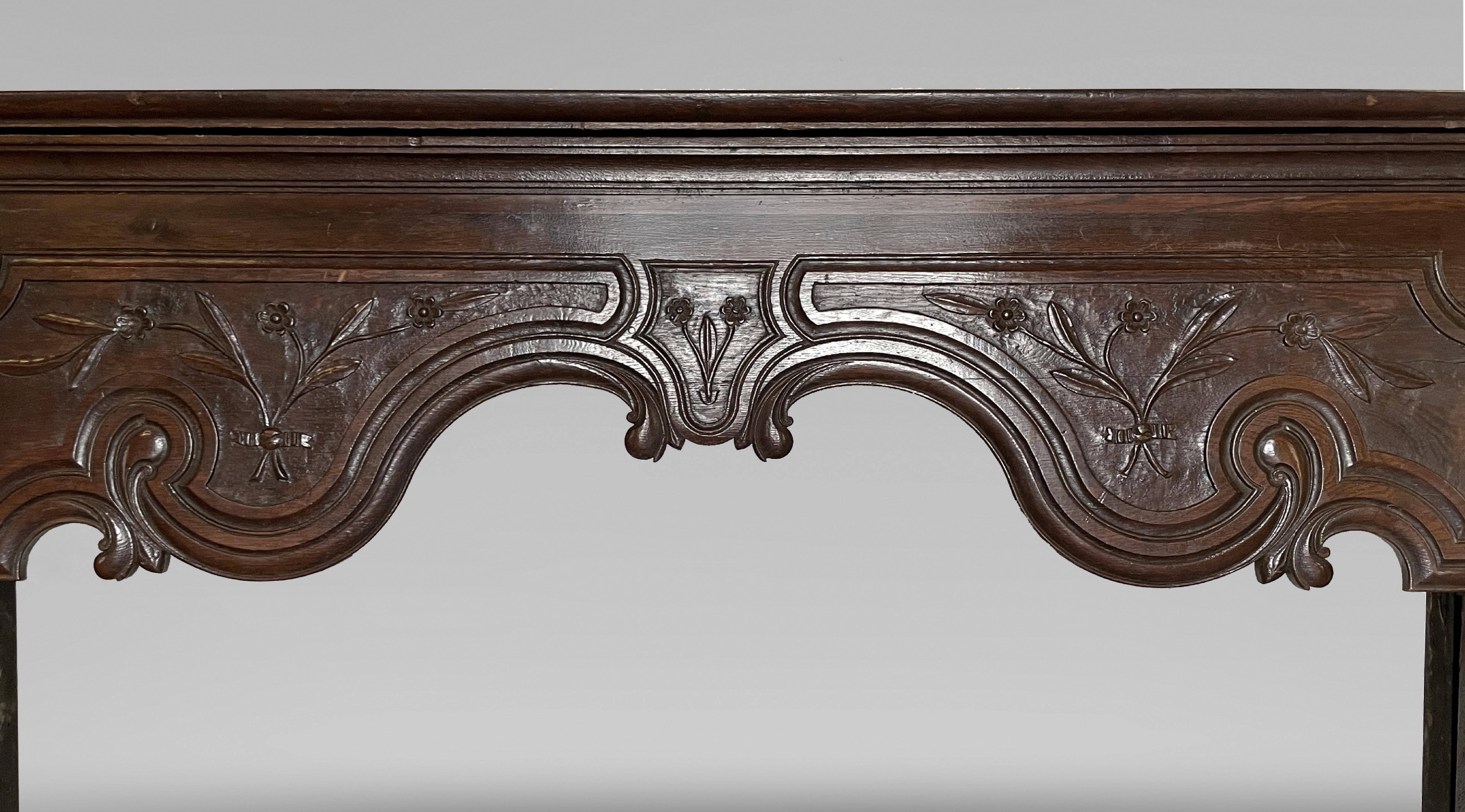 This antique fireplace from the 19th century is made from oak. The curved and graceful lines strewn throughout the piece are a classic attribute of the Louis XV style. Carvings of three bouquets of delicate flowers with their leaves are also added