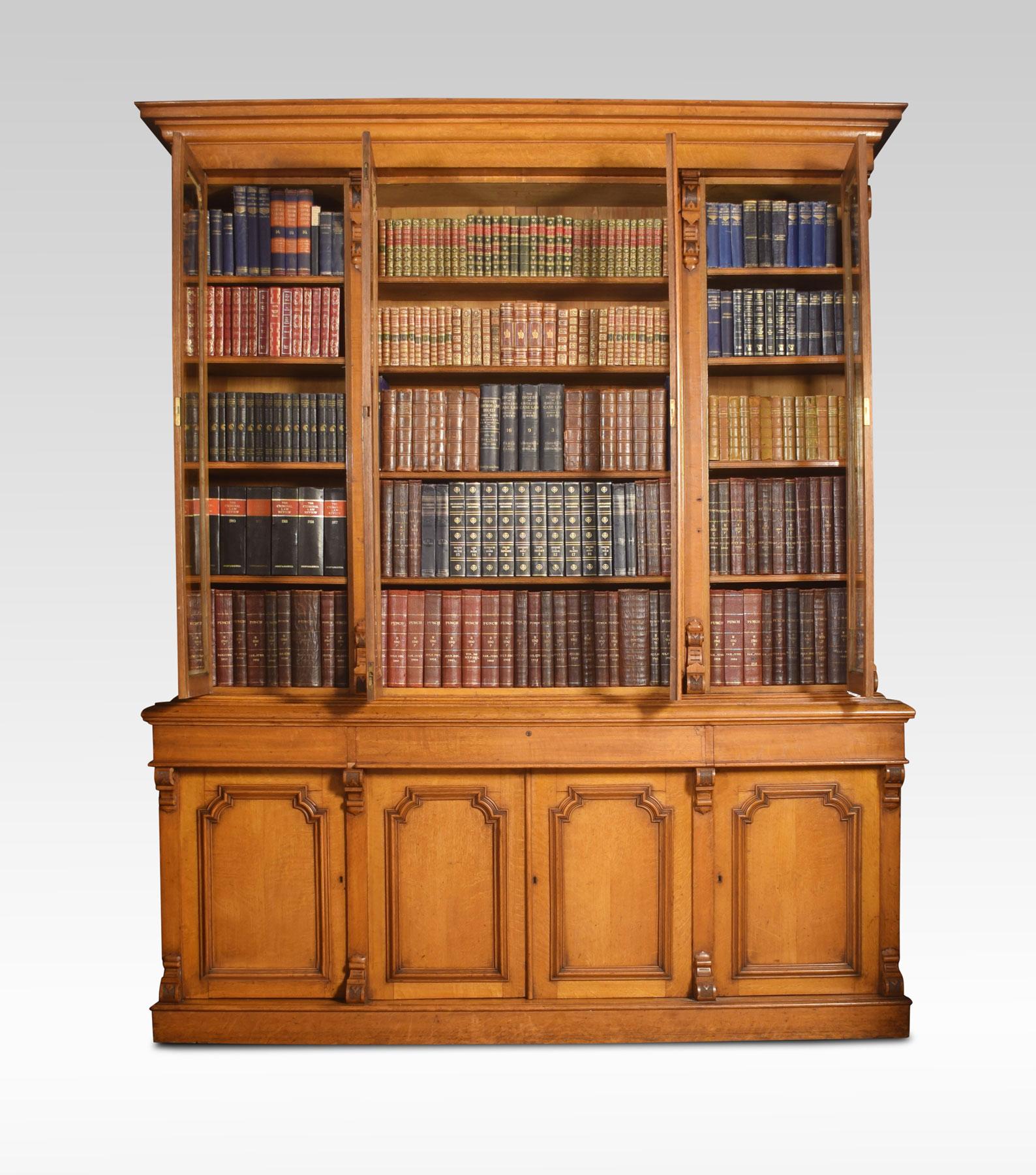 Large oak bookcase the moulded cornice above four large glazed doors each section having four adjustable shelves. The frieze fitted with three draws above the base section having four panelled doors opening to reveal shelved and fitted interior all