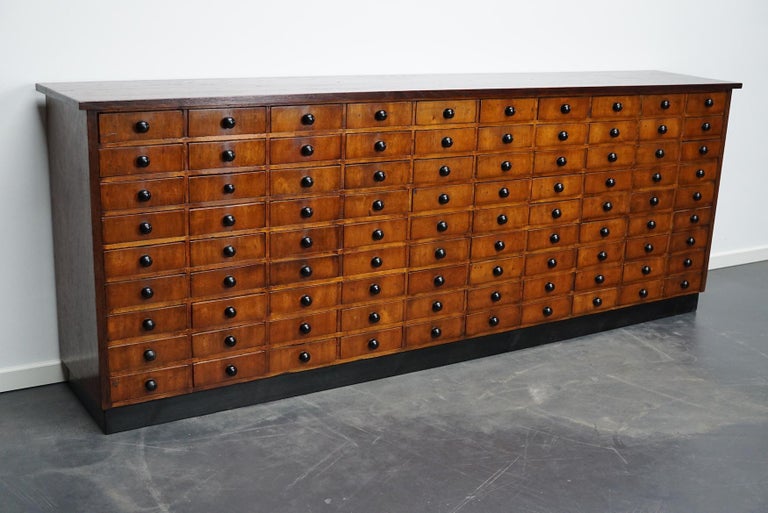This apothecary cabinet was made circa 1950s in Germany. It features 90 drawers with black knobs. The interior dimensions of the drawers are: D x W x H 36.5 x 20 x 6 cm, some of the drawers have dividers and some don't.