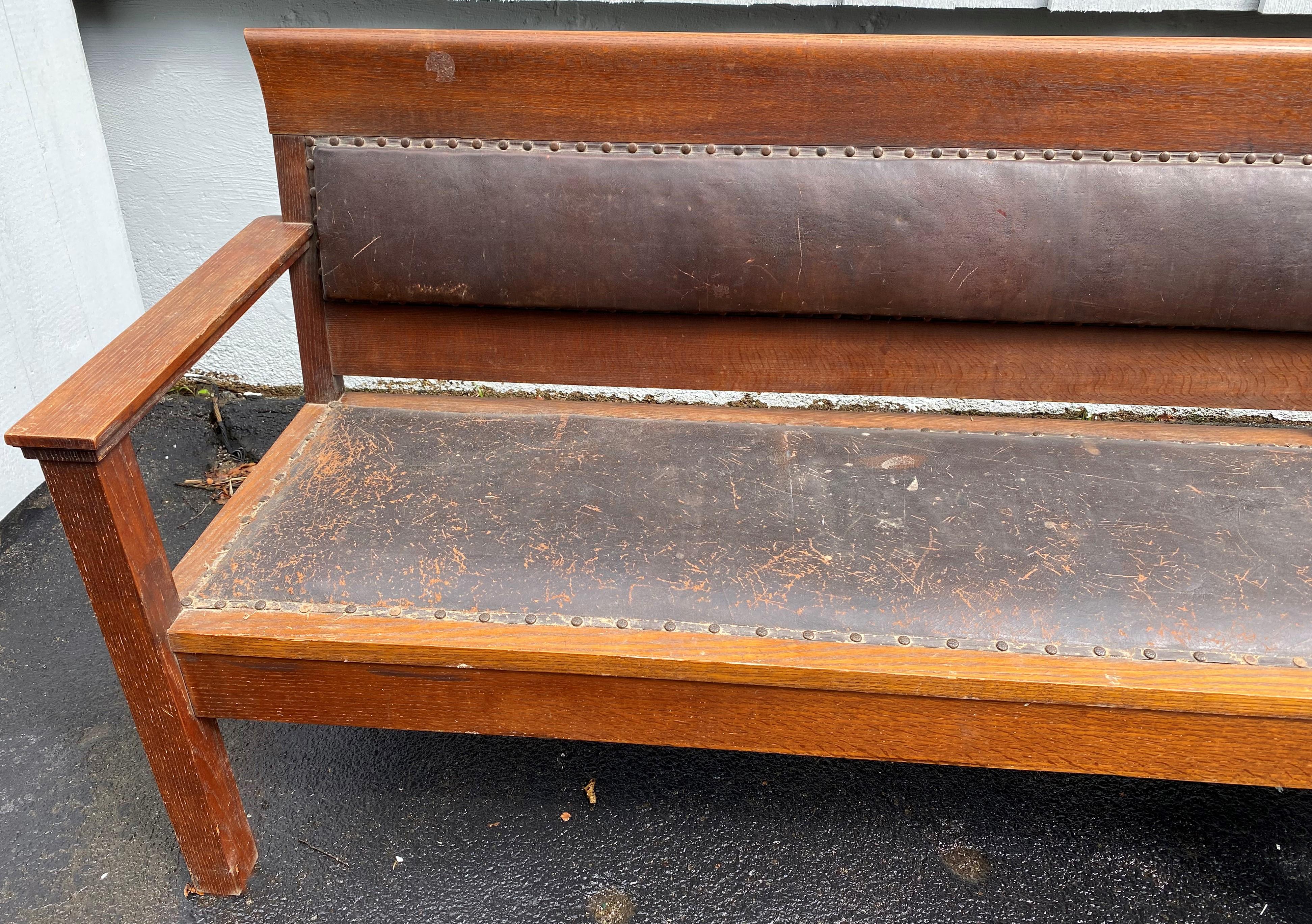 A nice example of a large oak railroad or train station bench with original nailed brown leather upholstered pads and seats, and original finish, supported by six legs. The bench dates to the late 19th or early 20th century in very good overall