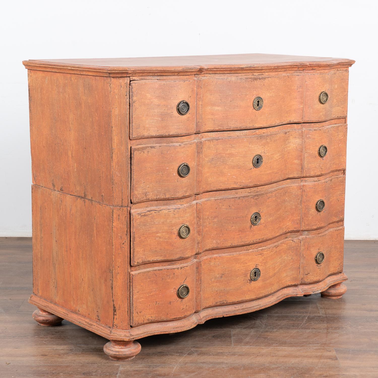 This rococo large oak chest of drawers features a serpentine front, brass hardware pulls and is raised on large bun feet.
The newer, professionally applied and layered salmon painted finish has soft white undertones and is gently distressed,