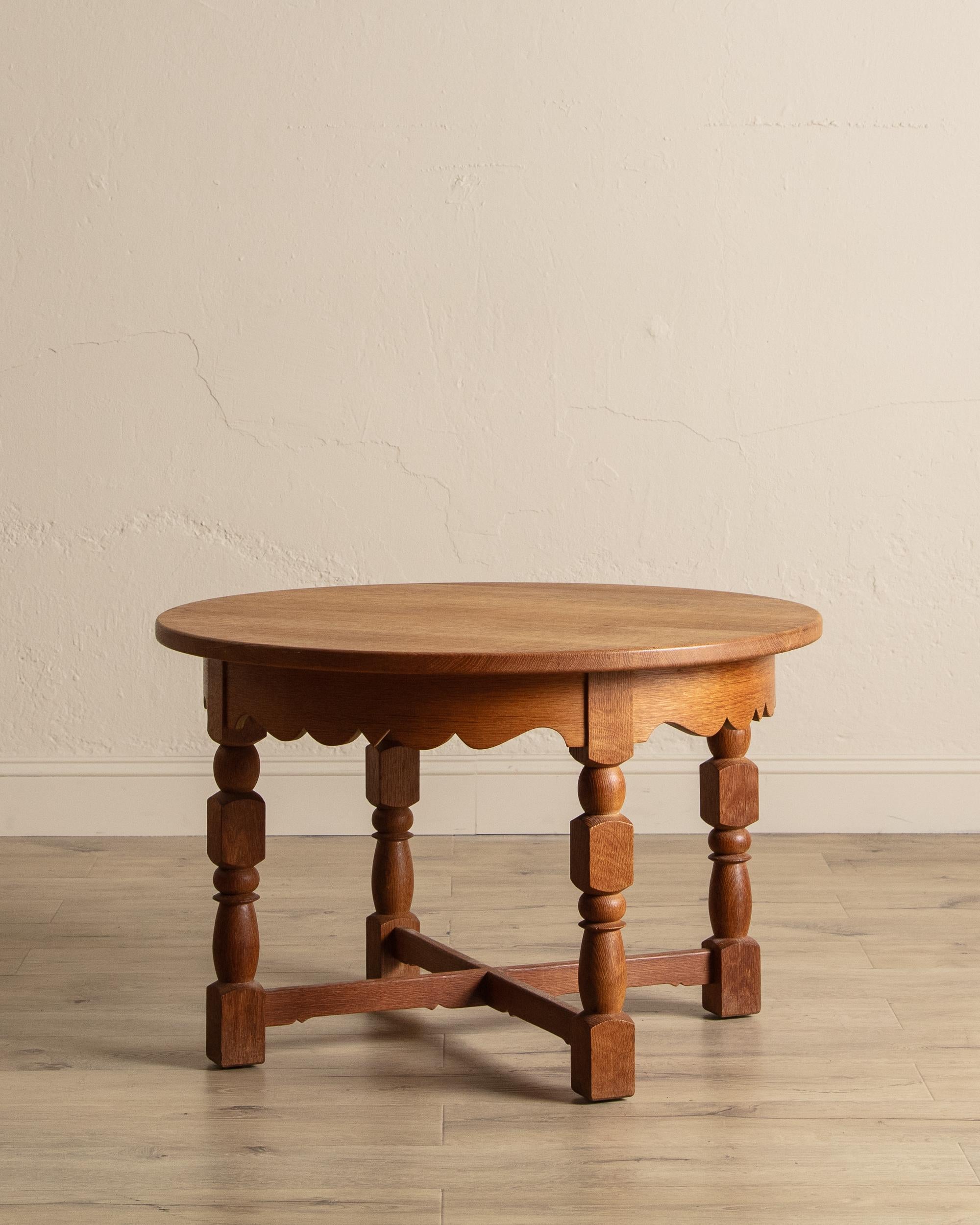 This large oak side table showcases a round top with a scalloped apron, finely turned legs, and a warm, inviting wood grain that highlights its classic craftsmanship. The elegant silhouette blends traditional charm with sturdy construction, making