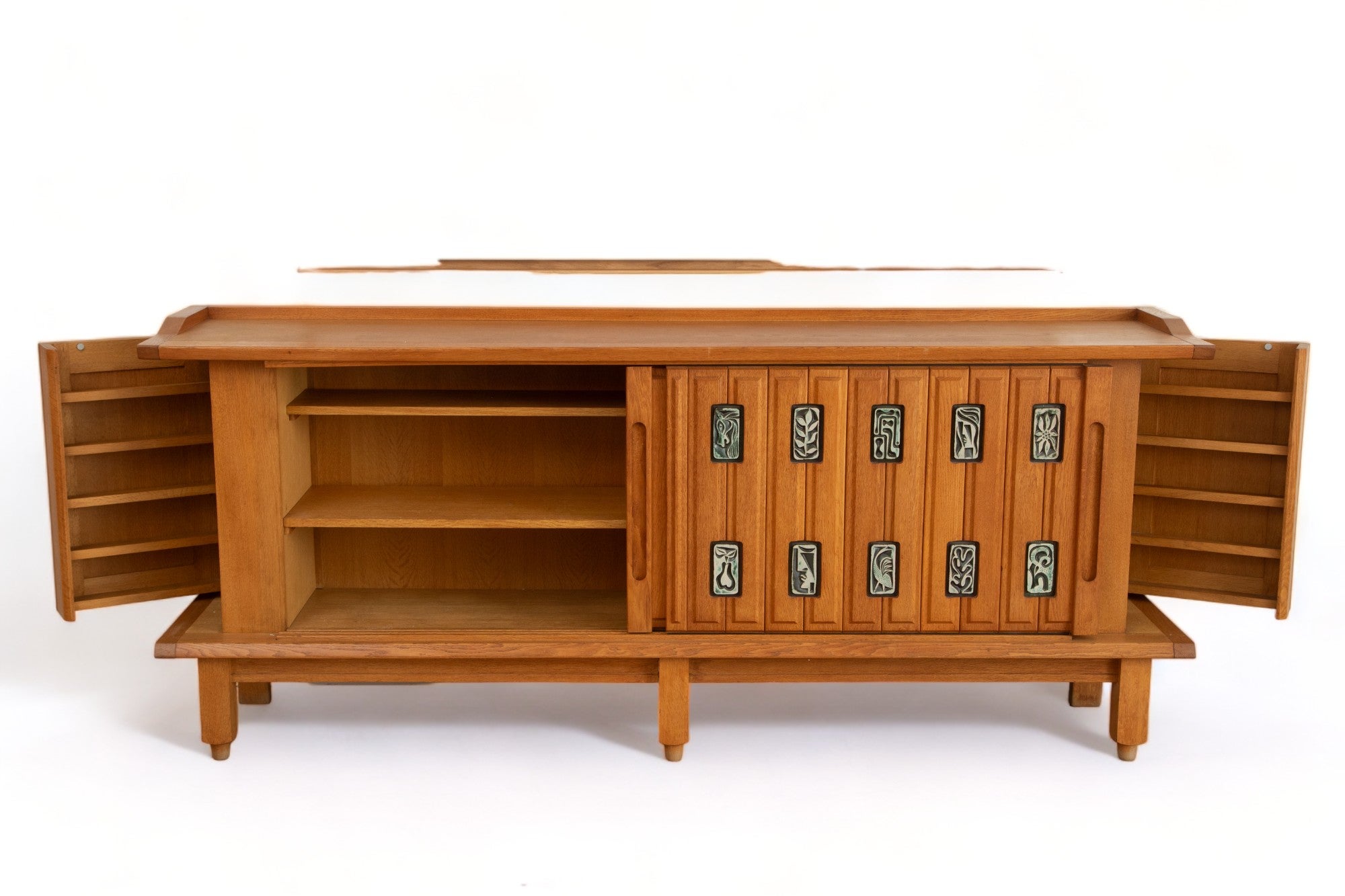 Large Oak Sideboard by Guillerme and Chambron 
Edition Votre Maison, France circa 1950-1960
 Opens with two sliding doors decorated by 20 glazed celadon and black ceramics by artist Boleslaw Danikowski
Concealing spacious storage with 2 shelves on