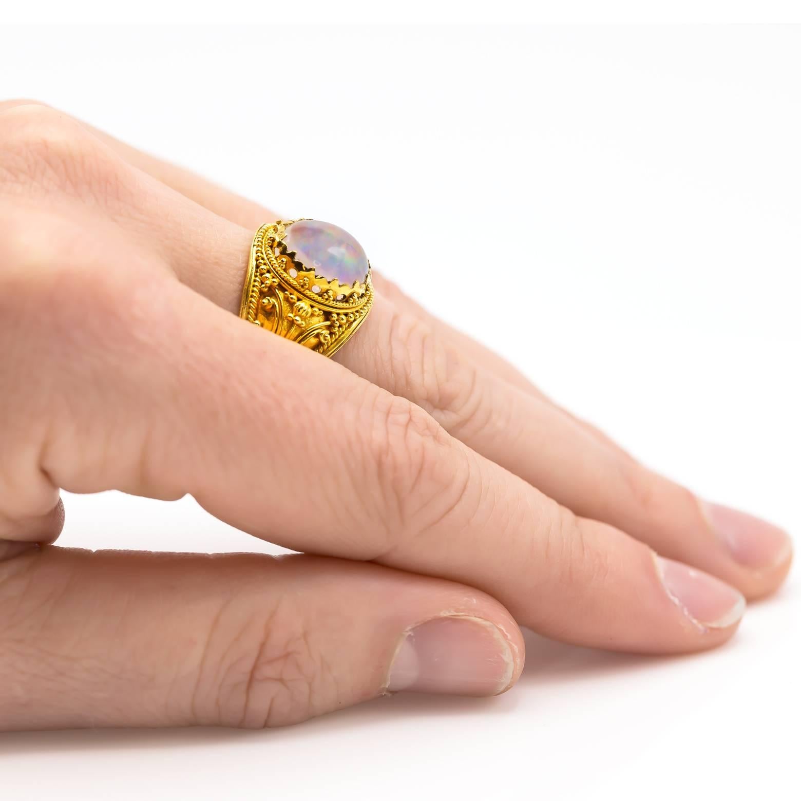 Dieser wunderschöne, verschlungene Jelly-Opal-Ring glänzt in 22 Karat Gelbgold. Detailliert und glänzend glänzt das Gold mit Spiralen und Wirbeln in traditioneller balinesischer Manier. Regenbögen spiegeln sich in diesem hellen weißen Cabochon-Opal,