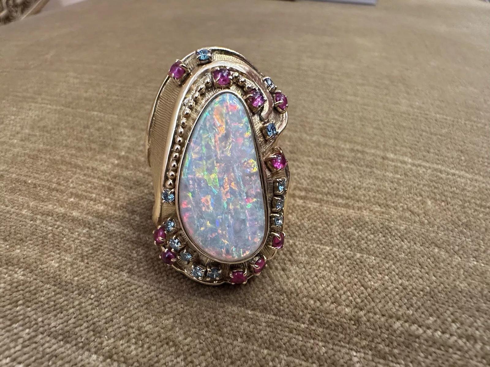 Grande bague en or jaune 18k avec opale, rubis et diamant 

La grande bague en opale et pierres précieuses présente une opale blanche allongée de 4,40 carats avec des jeux d'orange, de bleu et de vert, 10 rubis cabochons et 12 diamants bleus