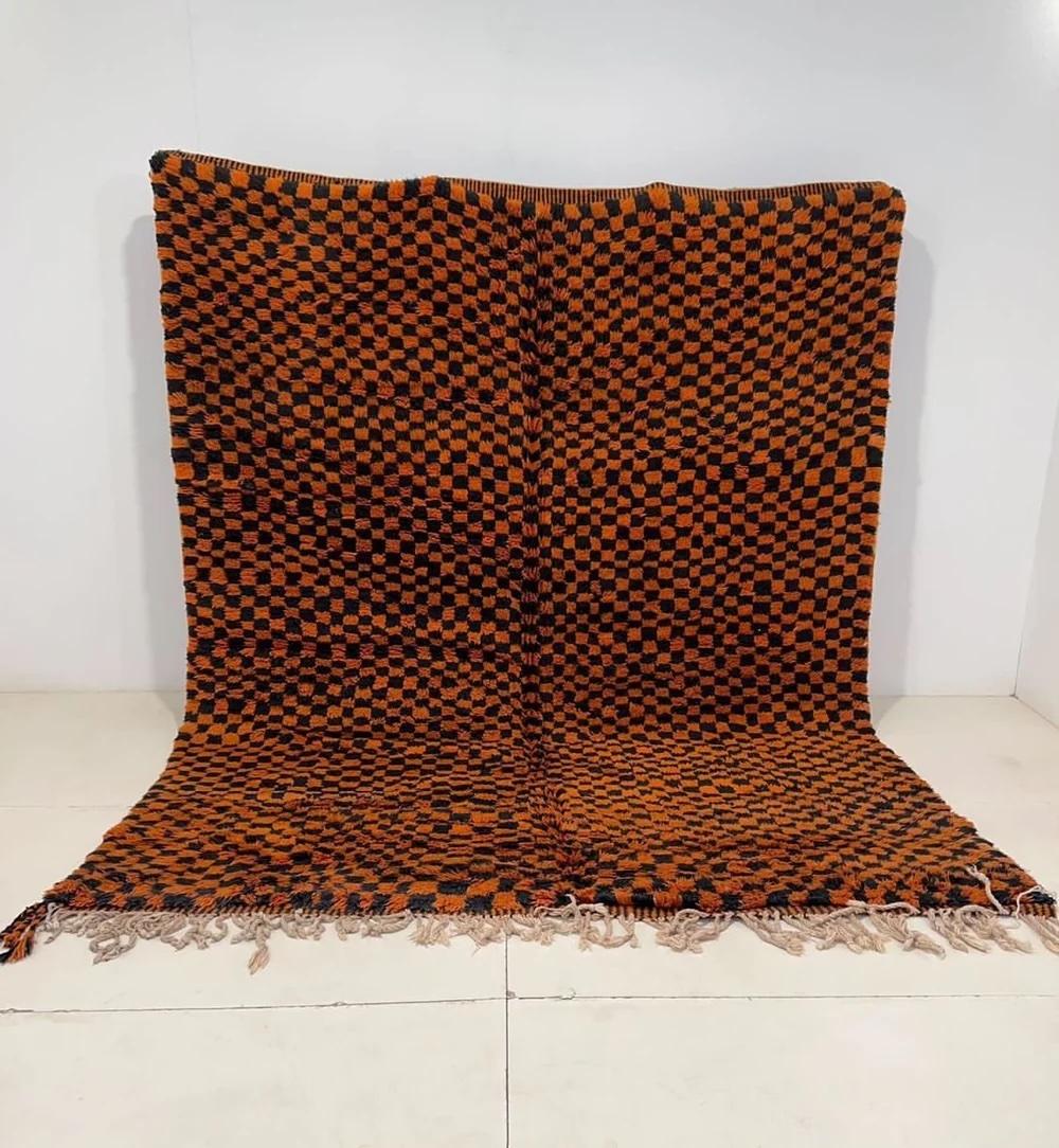 Questo grande e soffice tappeto marocchino tessuto a mano è stato realizzato da abili artigiani nelle montagne dell'Atlante. Presenta una base di lana arancione di alta qualità, riccamente colorata e con un motivo a scacchi neri. Realizzato a mano