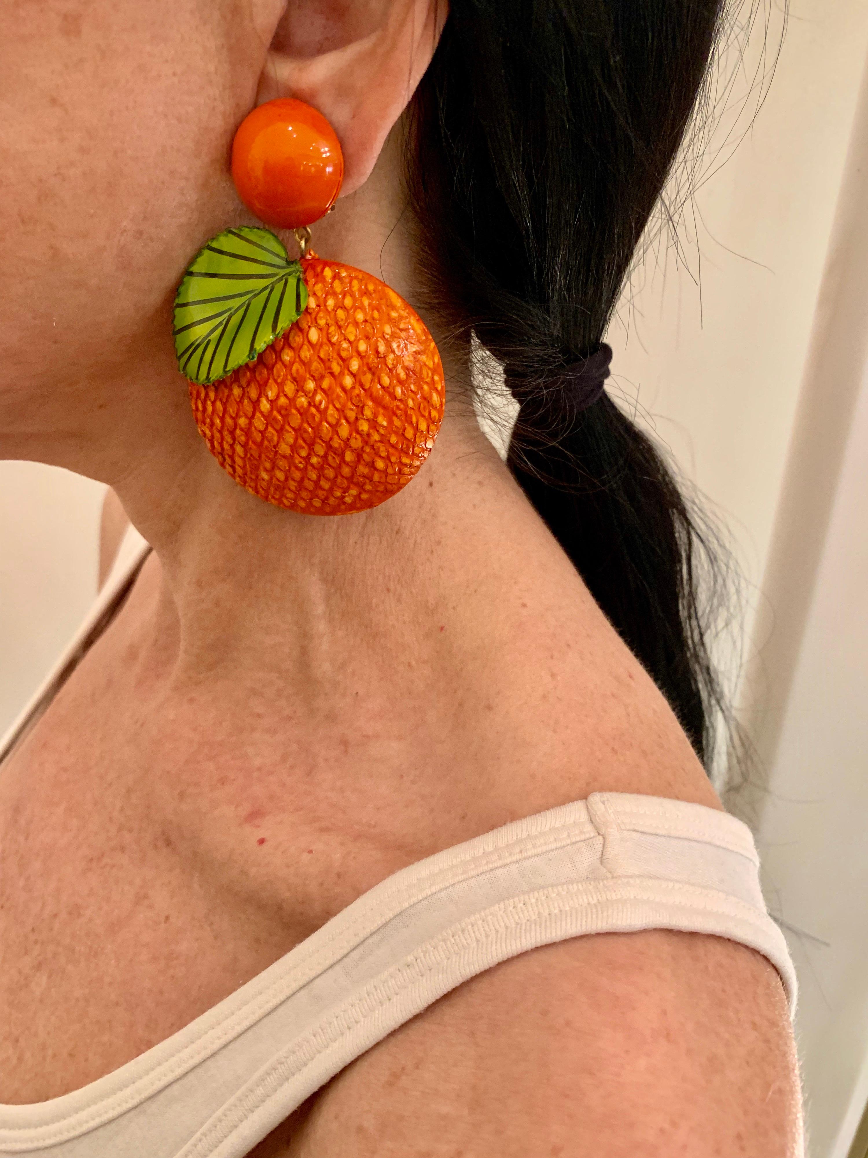 Light and easy to wear, these contemporary handmade artisanal clip-on statement earrings were made in Paris by Cilea. The lightweight earrings feature giant oranges, comprised out of enamel and resin. The orange has a three-dimensional hand