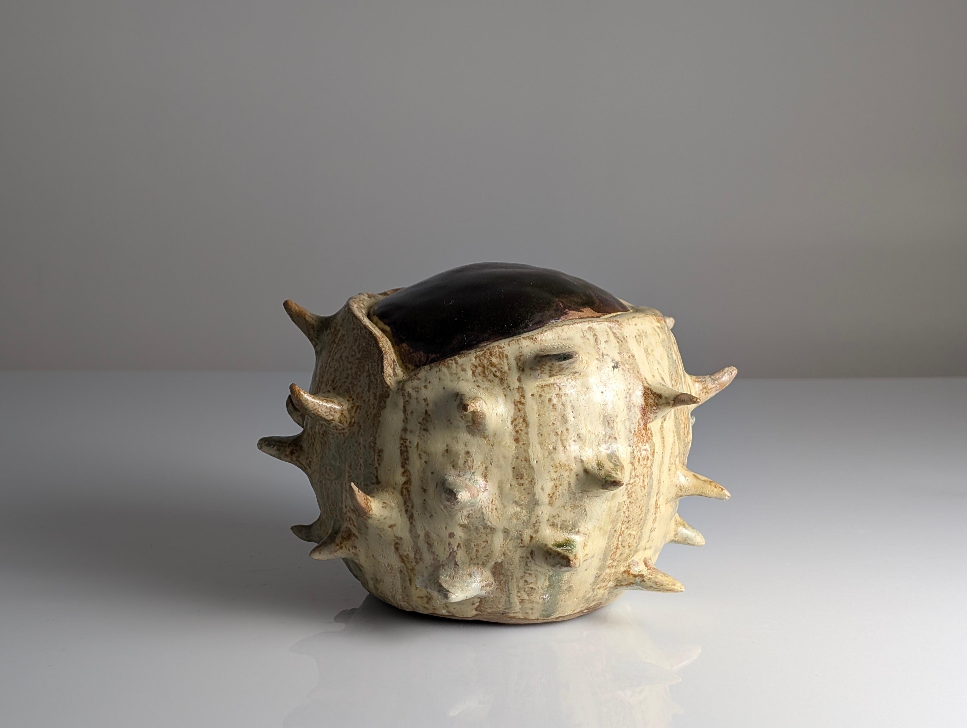 Questo pezzo scultoreo in gres del XX secolo è un distinto esempio di lavoro artigianale in gres, direttamente ispirato alla forma naturale di una bava di castagno. L'artista ha utilizzato abilmente smalti contrastanti per creare profondità visiva e