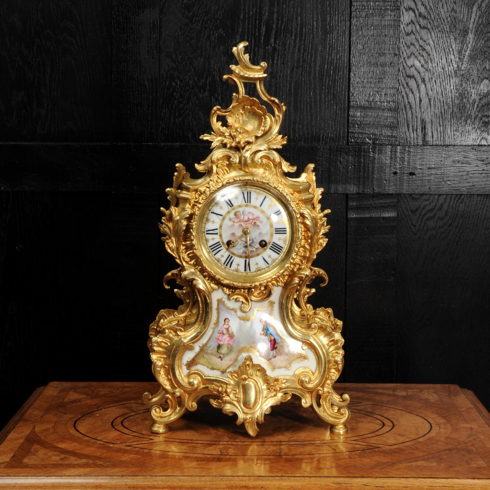 A large and beautiful antique French Rococo clock, circa 1900. Beautifully made in finely gilded bronze and mounted with exquisite Sèvres style porcelain. Porcelain has a white ground with panels delicately painted with scenes. Below the dial the