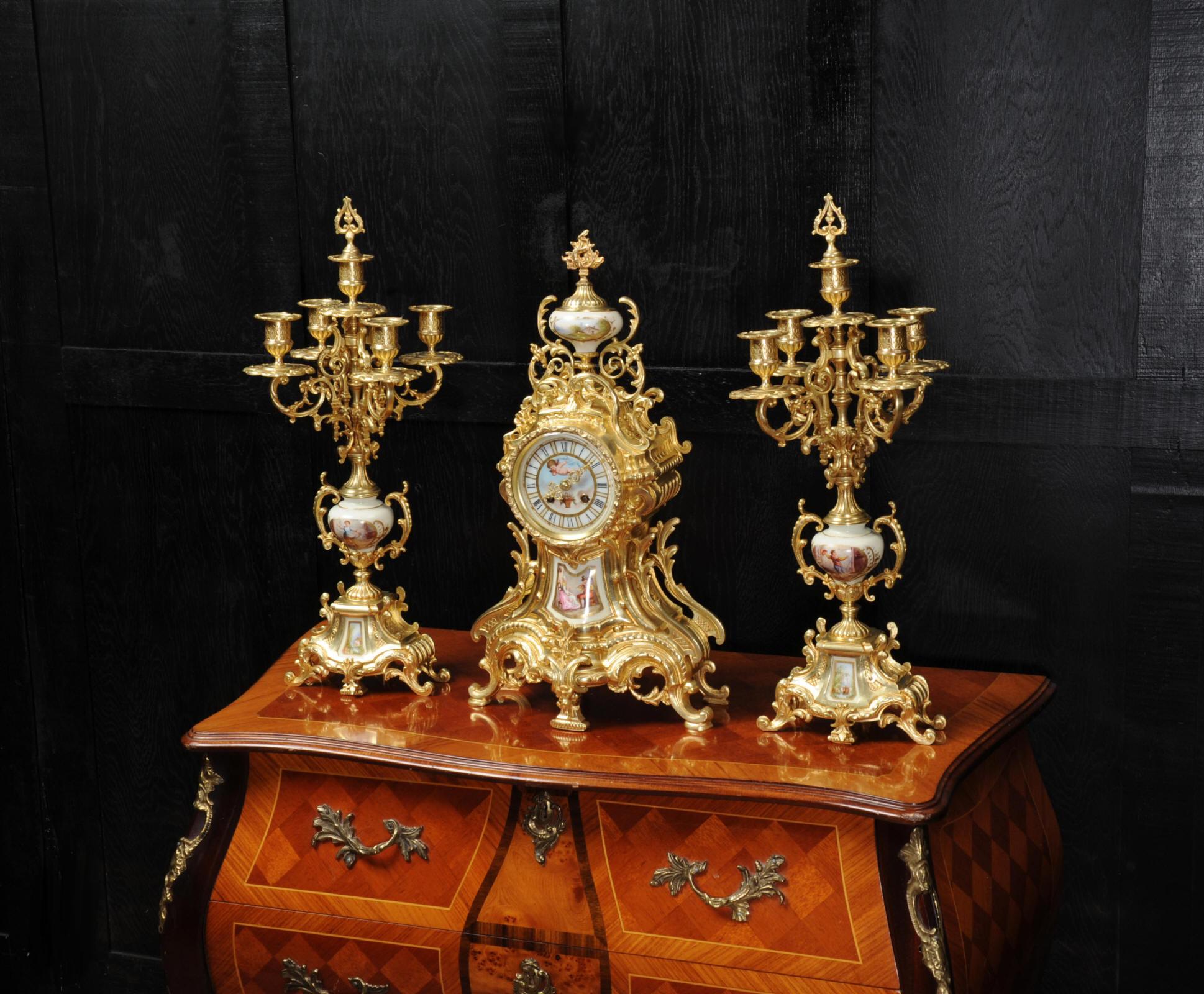 A large and beautiful antique French Rococo clock set circa 1900. Beautifully made in finely gilded bronze and mounted with exquisite Sèvres style porcelain. Porcelain has a white ground with panels delicately painted with scenes. The urn shows an