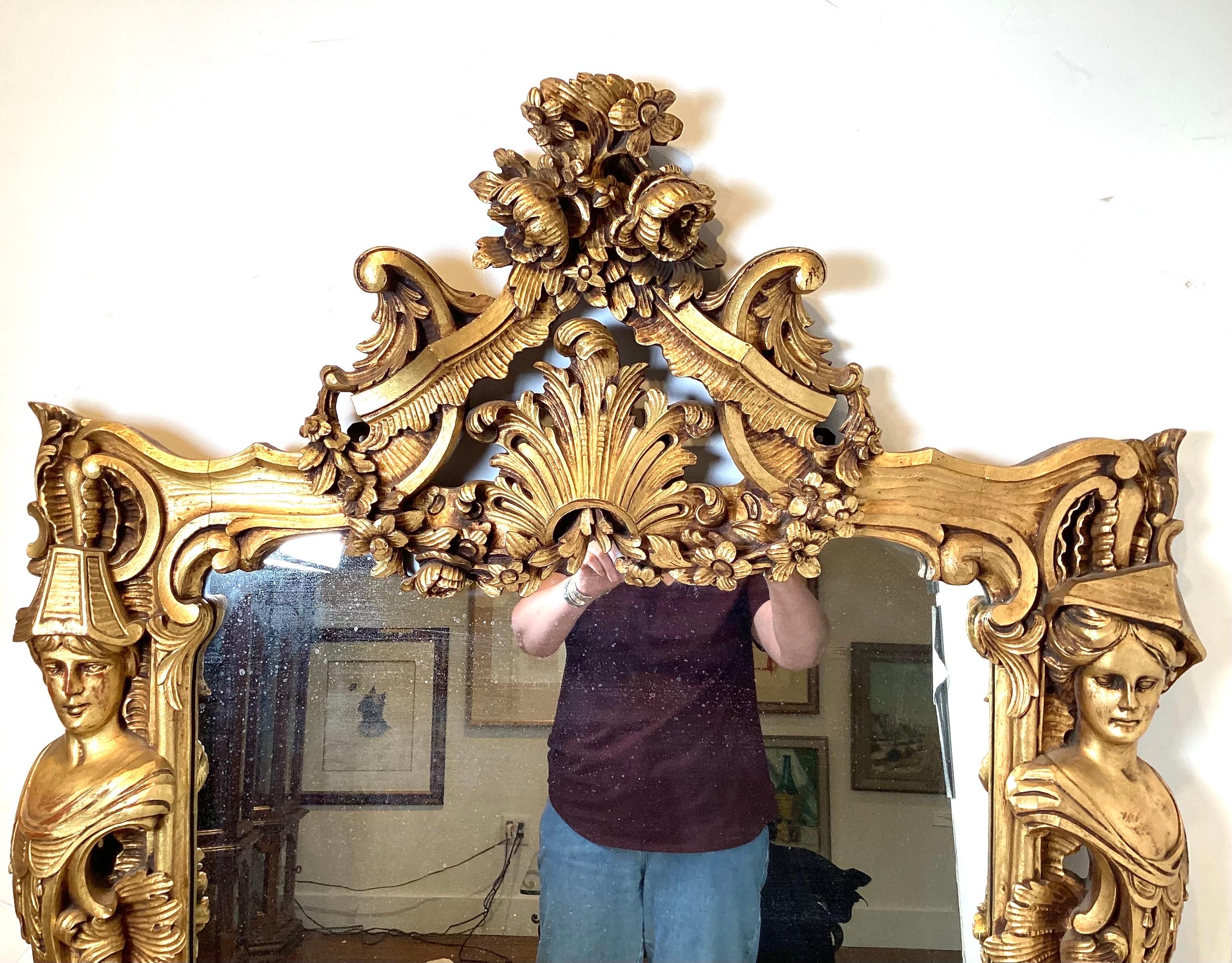 An elaborate and ornately carved walnut and gilt framed mirror. The high pediment with plume and flowers with caryatid decoration at the sides. The mirror with all silvering intact, retains is Christies label. European, France or Italy, early 20th