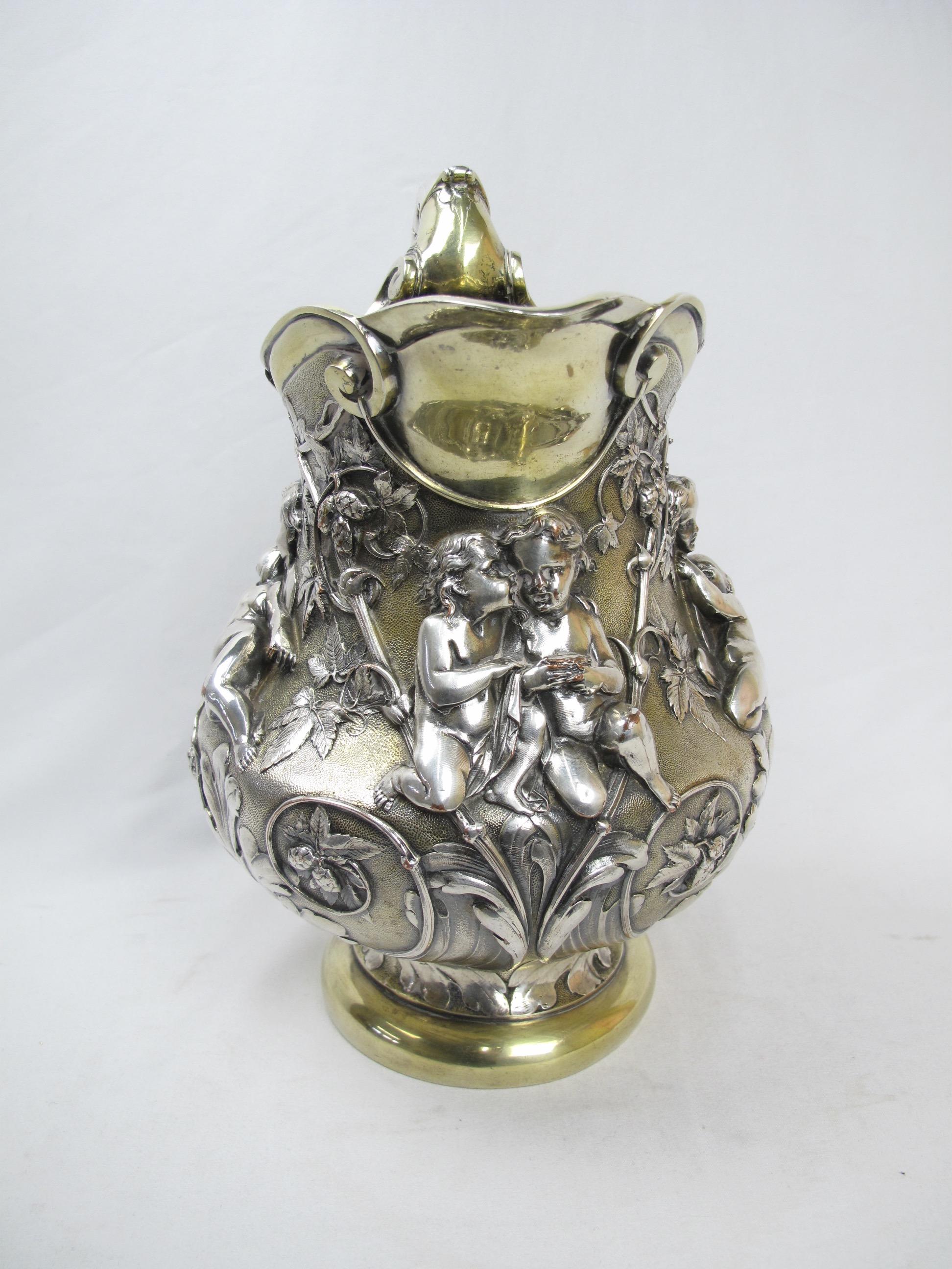 Large Elkington repousse silver-plate pitcher featuring four 'scenes' with putti (a representation of a naked child, especially a cherub or a cupid) cavorting among laden hop vines and leaves. Silver plate with brass brightwork over copper and a