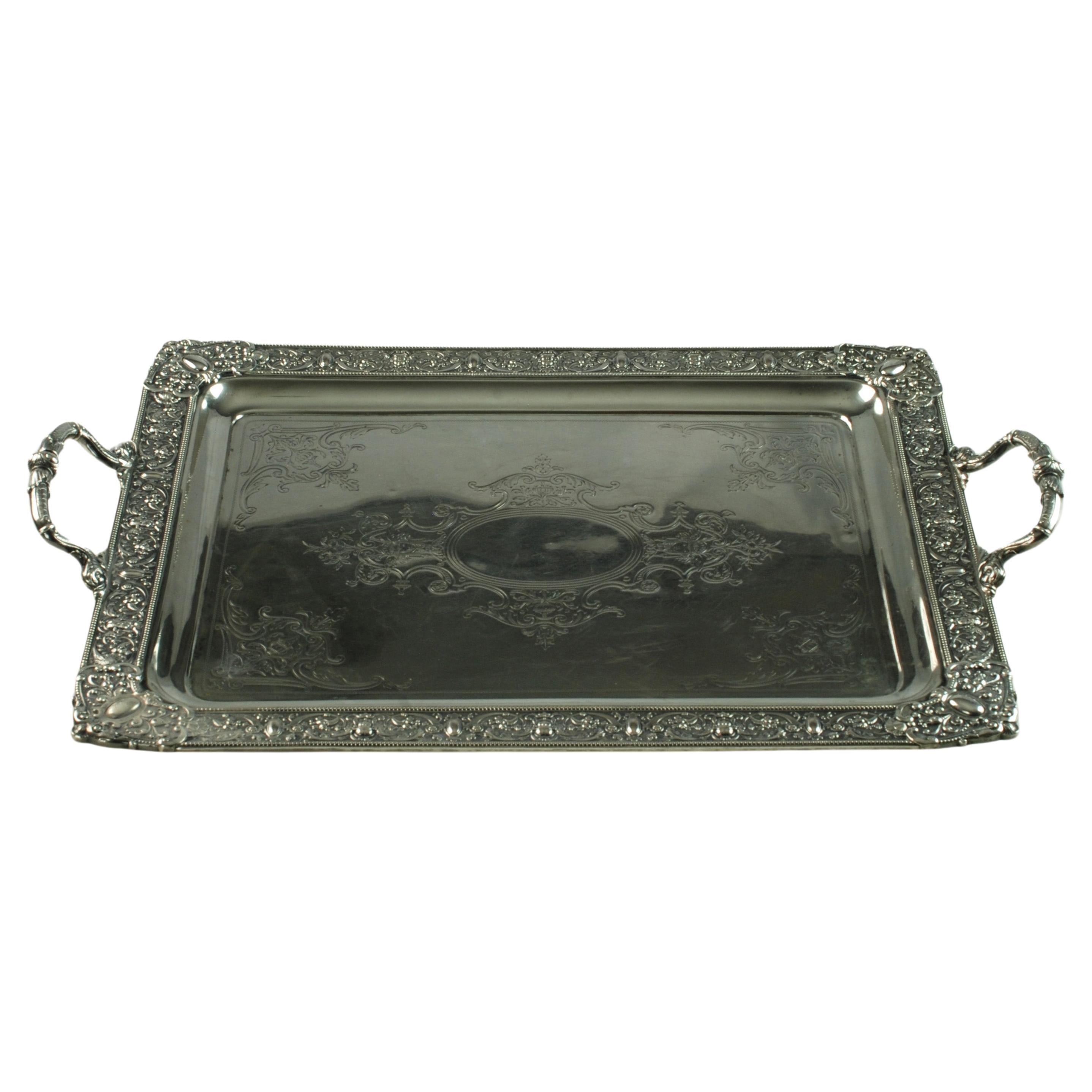 This elegant sterling silver rectangular double-handled butlers tray features engraved Neo-Renaissance decoration including winged cherubs along with urns and floral and foliate motifs.  There is a large oval cartouche at the center which has not