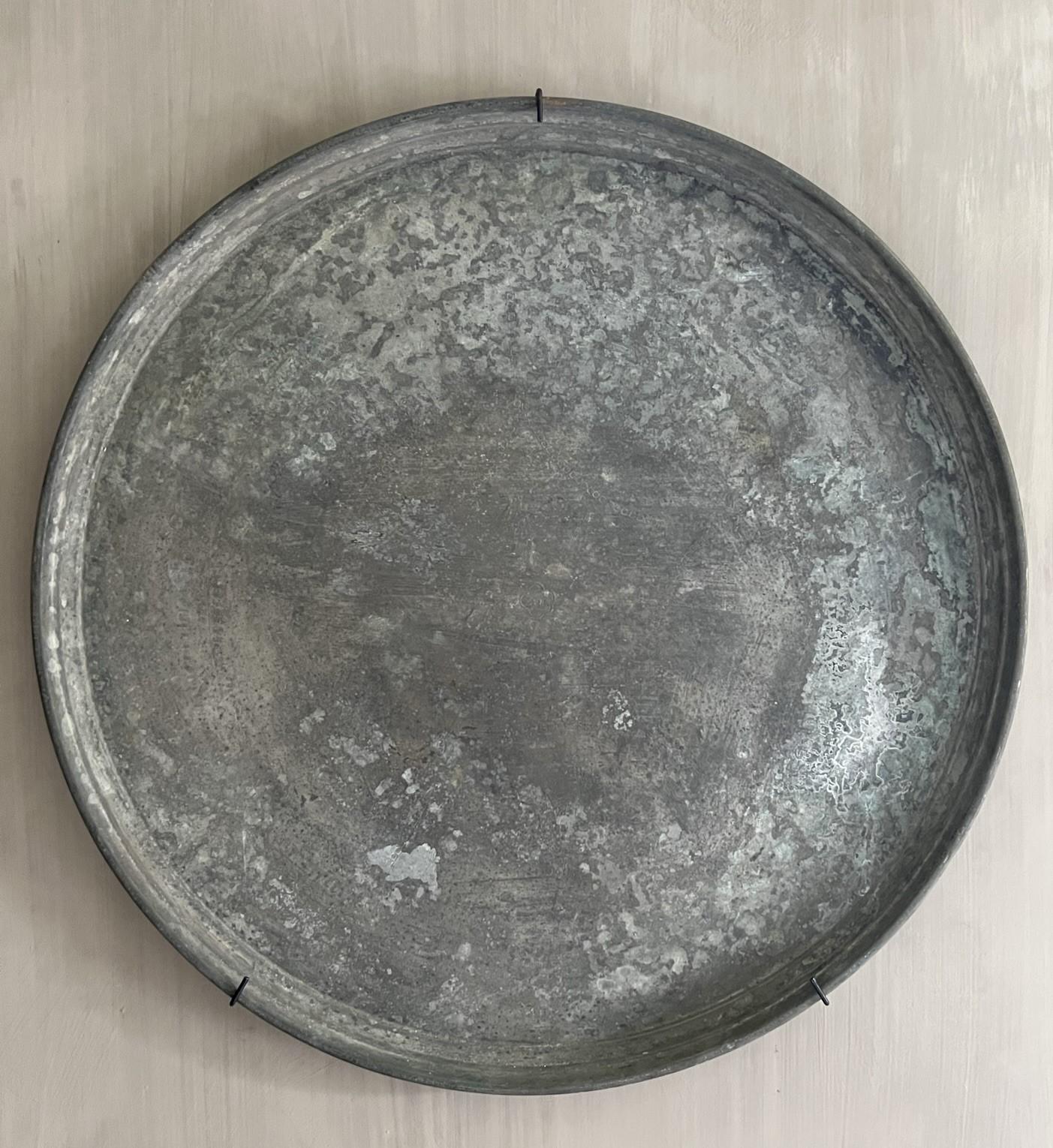 A LARGE OTTOMAN TINNED-COPPER TRAY

Of circular form, the engraved decoration consisting of a central medallion with radiating foliated patterns very good condition overal. Beautiful silver green patina. Mounted on a wall it has the attraction of a