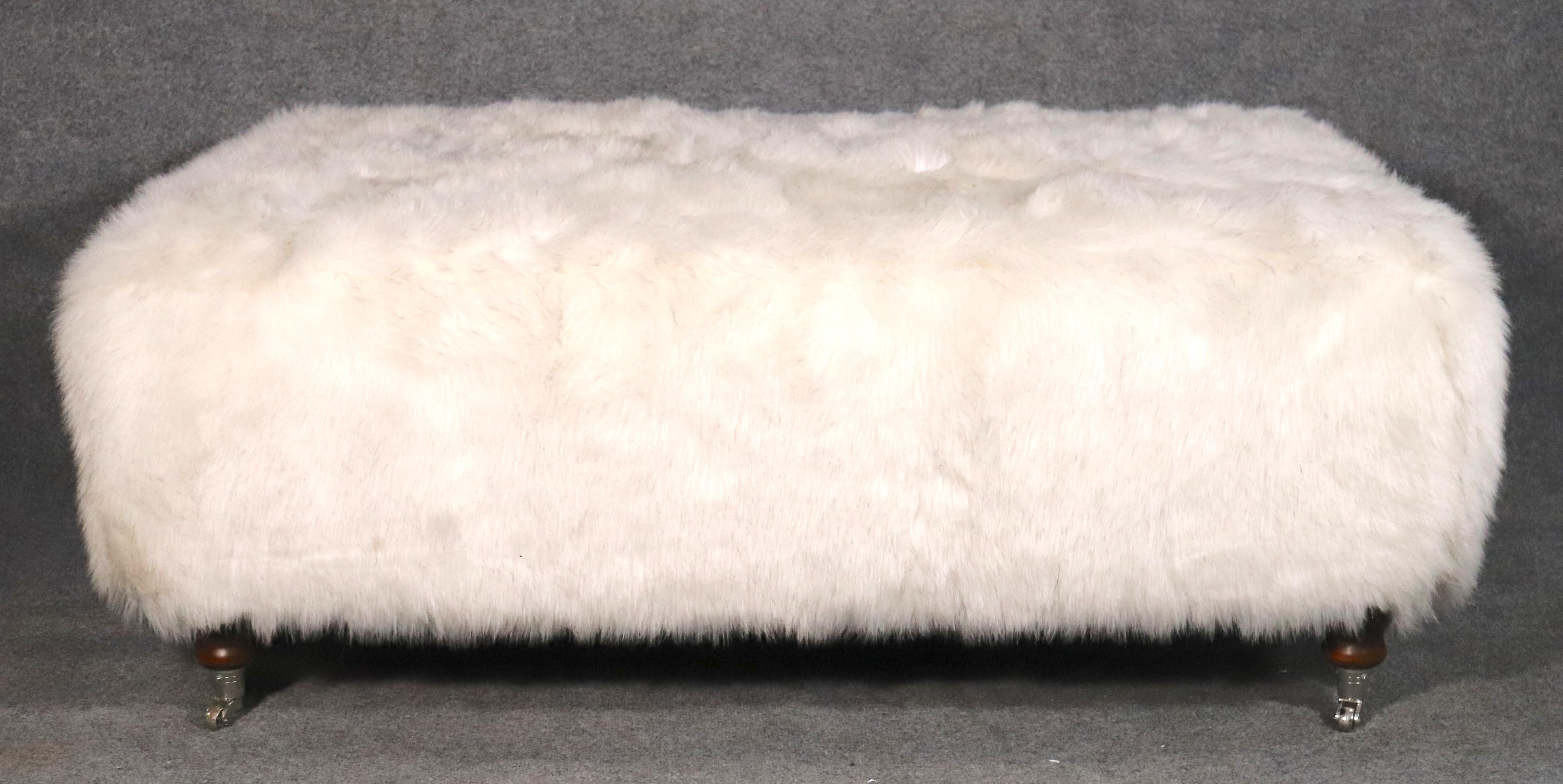 Large faux fur footstool with wood legs on casters. 
Please confirm location.