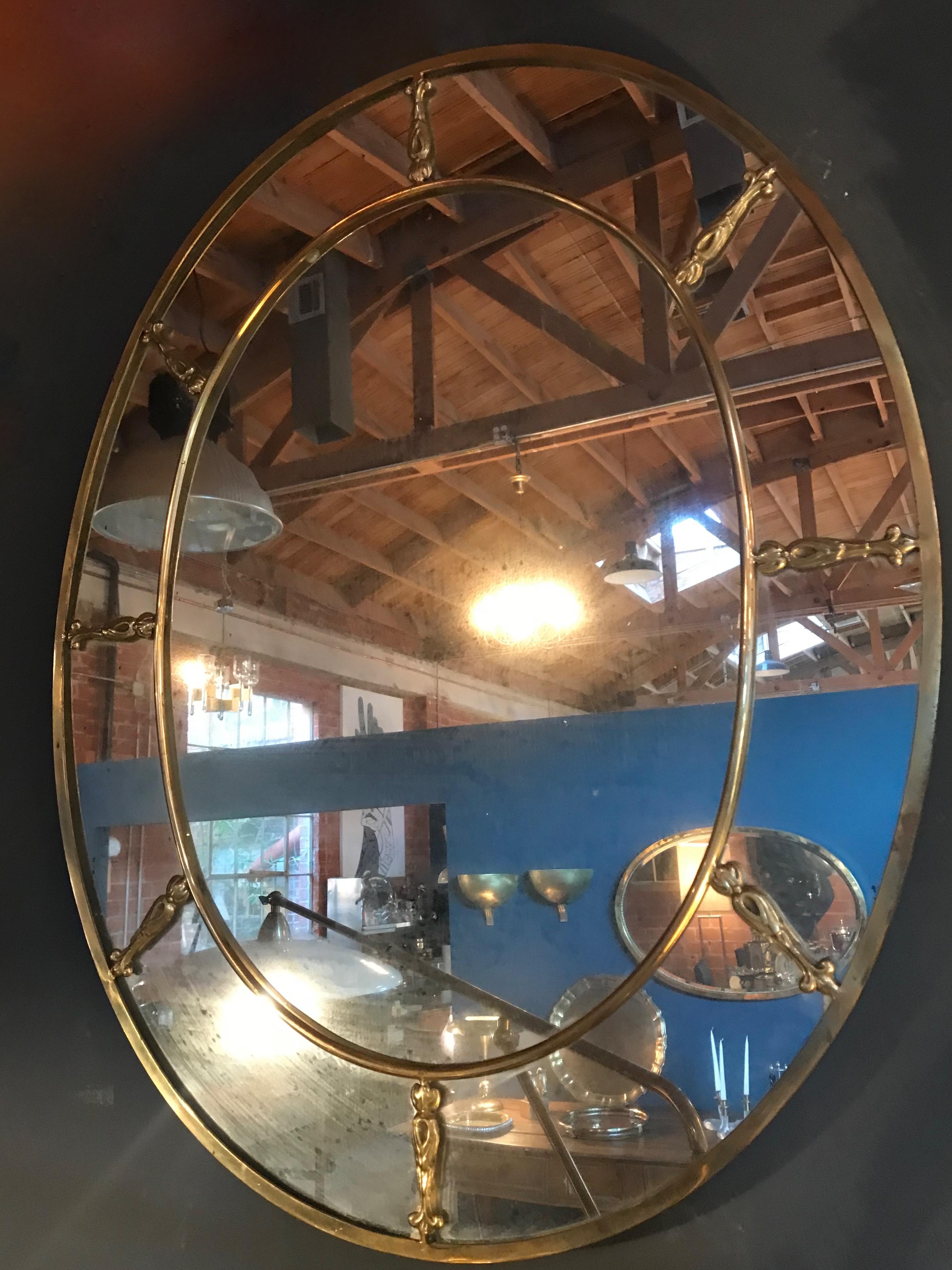 Large oval brass Art Deco mirror from the 1930s. A thick solid brass rim (1.5 inches ) with golden bronze decorative elements applied on the mirror and a continuous brass 