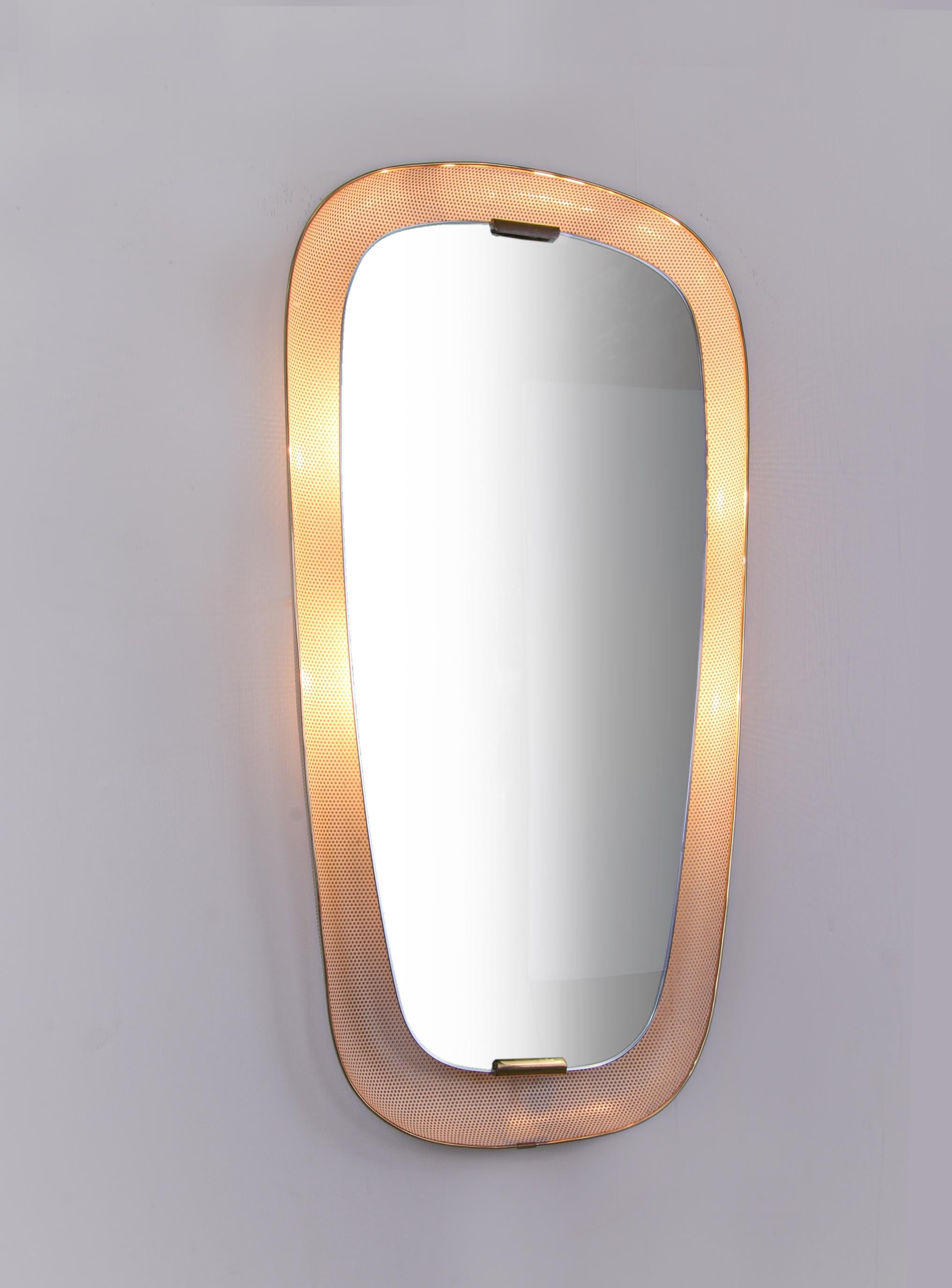 Elegant wall mirror with illuminated background. Manufactured in Germany, 1950s. 
 
The frame is made of perforated sheet metal with brass hardware. 
 
Measures: height 31.9” in. (81 cm), width 16.5” in. (42 cm), depth 2.75” in. (7 cm). 
Lighting: