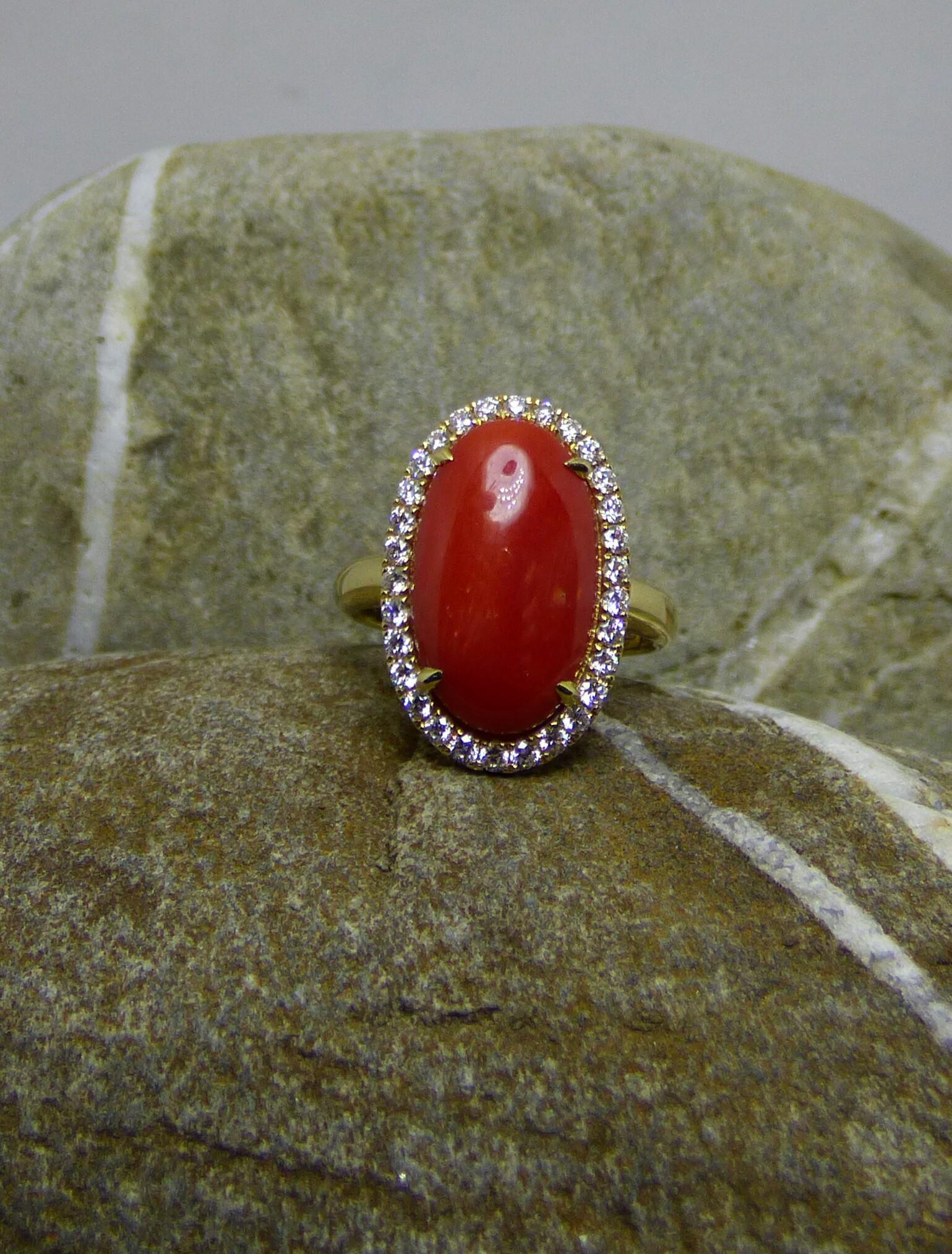 A large oval natural red coral cabochon (5.57ct.) is surrounded by thirty Diamonds with a total weight of .50ct. The ring is handmade in 14K yellow gold ring. It is hallmarked at the Dublin Assay office.  This beautiful ring truly fills the finger!