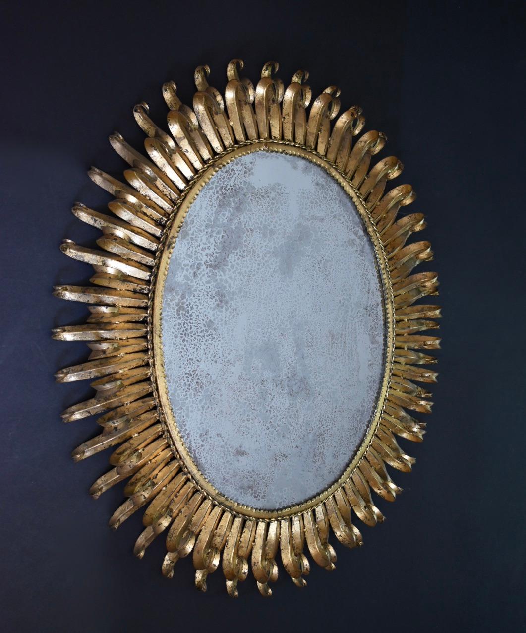 Large size oval soleil or sunburst wall mirror in original gilt iron finish with two rows of alternating long and short eyelash rays. Mirrored glass has heavy antiquing to the silvered backing. Single steel loop at back allows for vertical hanging.