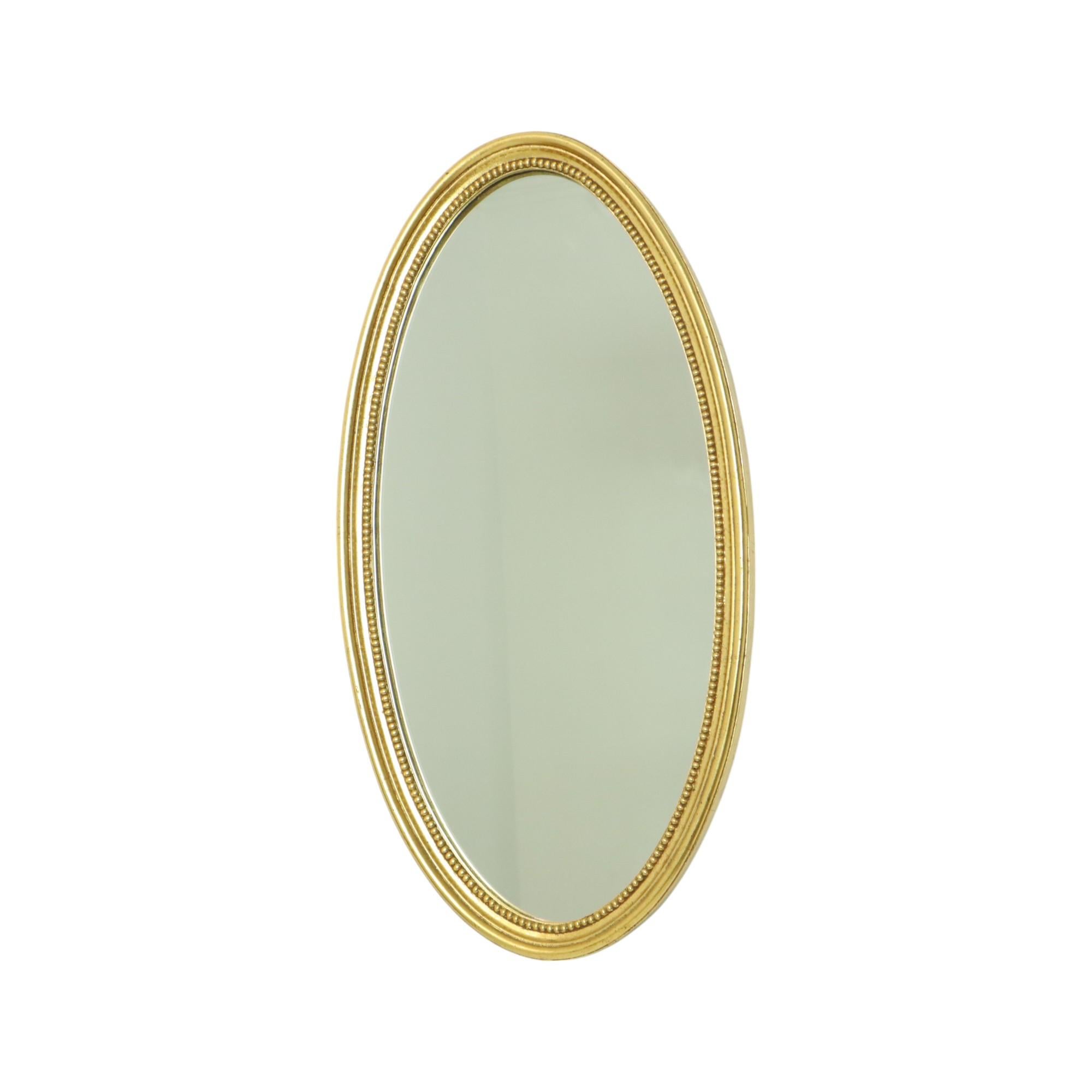 Large oval mirror in neo-classical or Hollywood Regency style, made of gold-colored resin and wood, circa 70s.

A very stylish and nice mirror with a classic frame decorated all around with a dot pattern, the gold-colored layer carries a beautiful