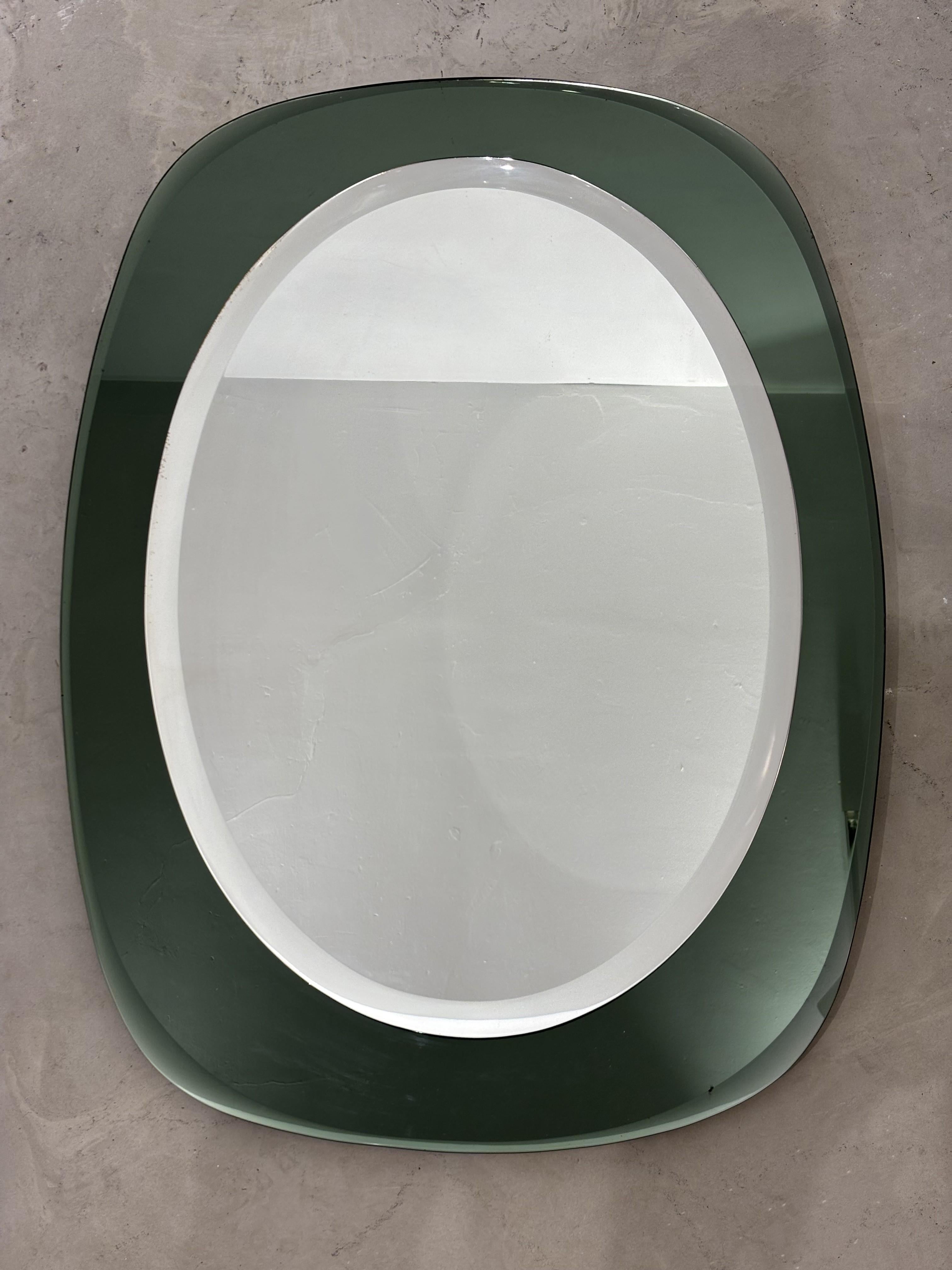 Large oval Italian mirror by Cristal Art. The originality of the technique lies in the frame made of a thick layer of glass lined with a mirror surface on its back: the frame is also reflective and the emerald green color of the glass reacts to