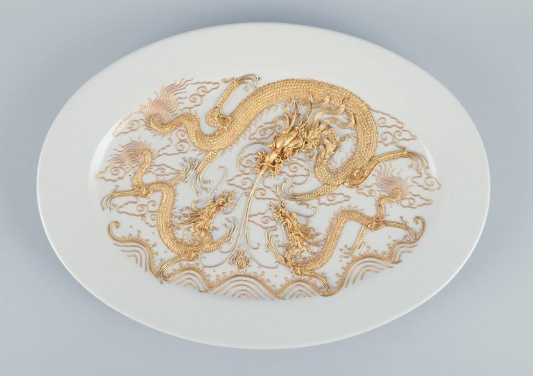 Großer ovaler Porzellanteller mit Drachenmotiven.  Im Stil von Versace.
Mit vergoldetem Metall verziert.
Ab etwa 1980.
In ausgezeichnetem Zustand mit minimaler Abnutzung.
Abmessungen: Länge 41,0 cm x Tiefe 29,5 cm x Höhe 3,0 cm.