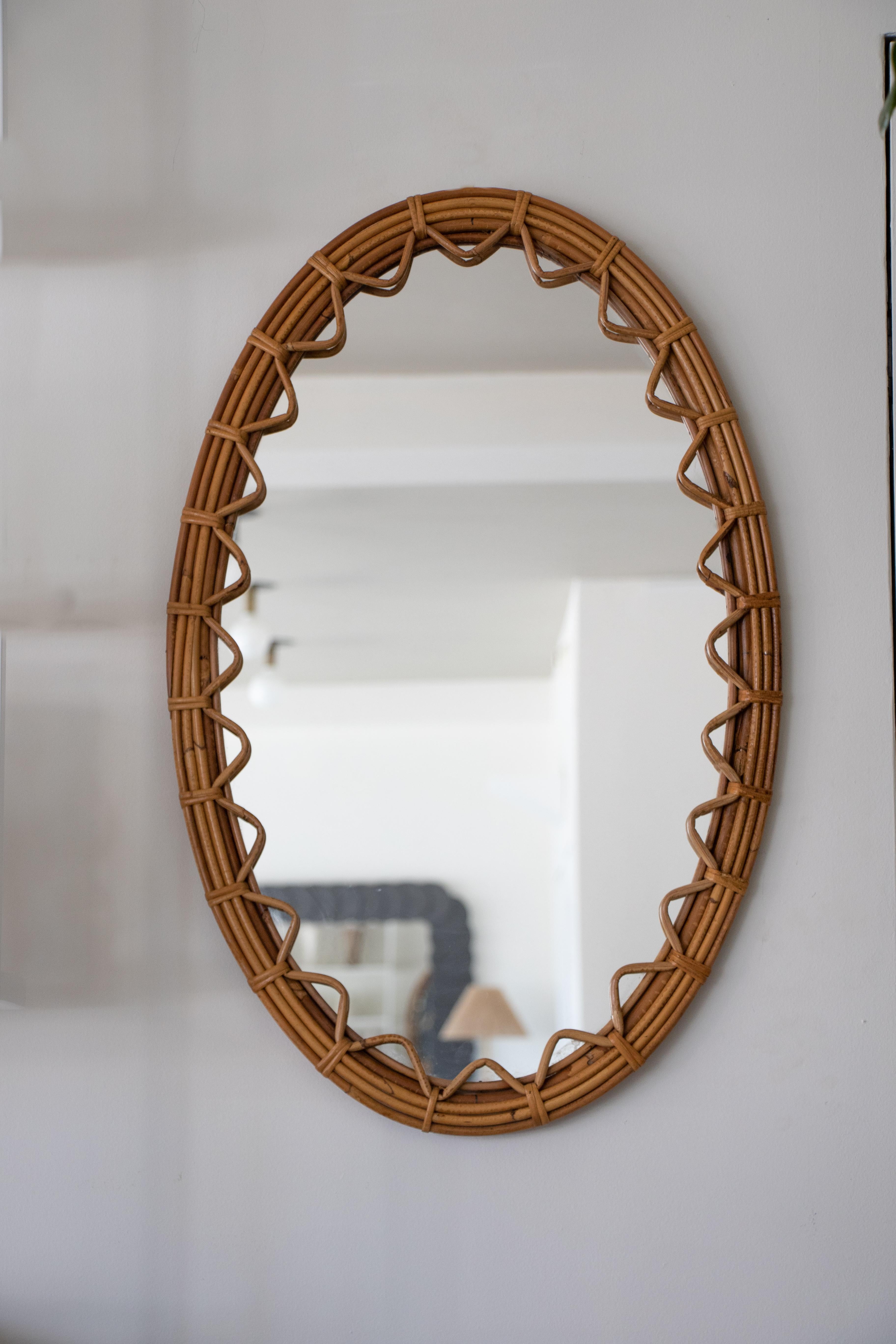 Beautiful large rattan mirror in an oval shape from Spain, 1960's. Unique design with zig-zag rattan detailing encompassing the mirror. Great size, perfect for bathroom or entryway. Nice vintage condition with original rattan frame and newly