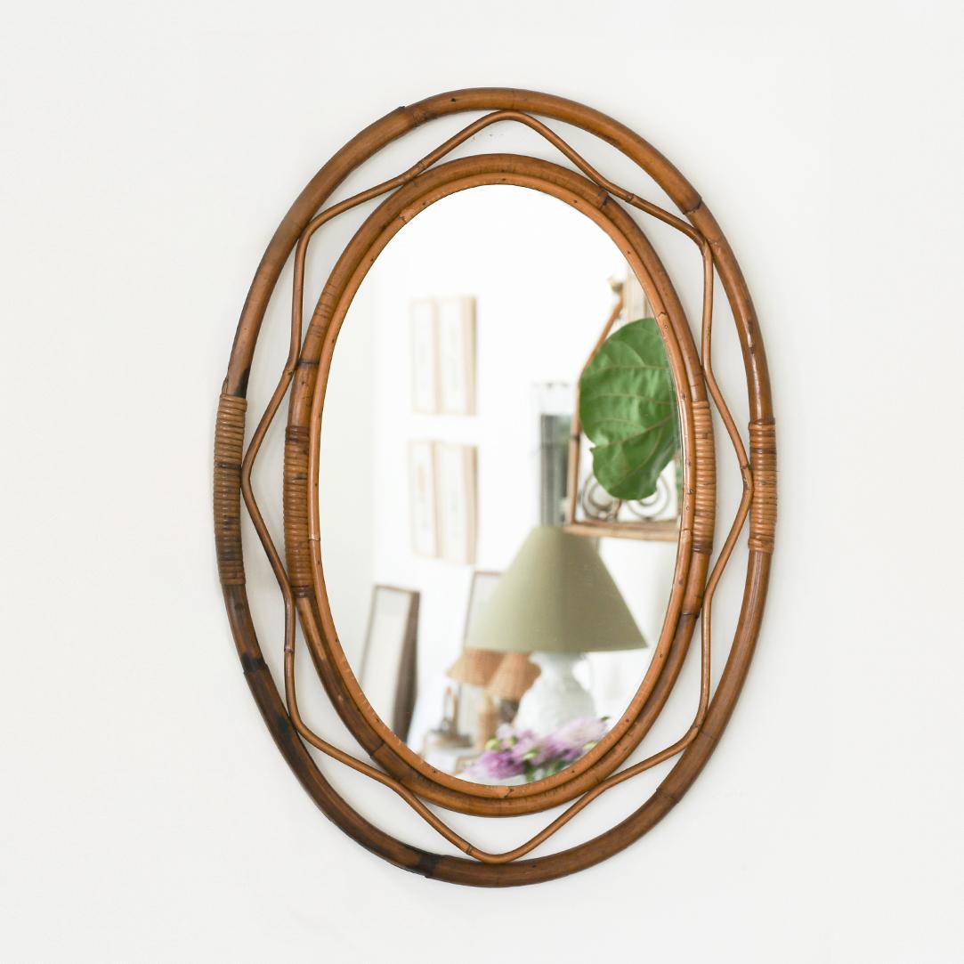 Beautiful large rattan mirror in an oval shape from Italy, 1960's. Unique design with wavy rattan detailing encompassing the mirror. Great size, perfect for bathroom or entryway. Nice vintage condition with original rattan frame and mirror.