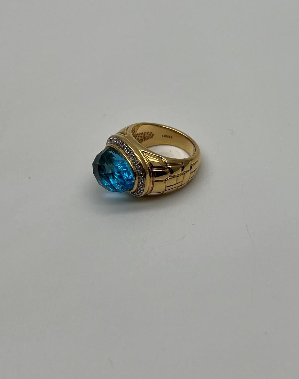 This exquisite piece features a bold design in yellow gold. The centerpiece is a large, faceted Swiss Blue Topaz, set in a bezel that enhances its vibrant color. Surrounding the stone is a halo of small, sparkling diamonds, adding a touch of